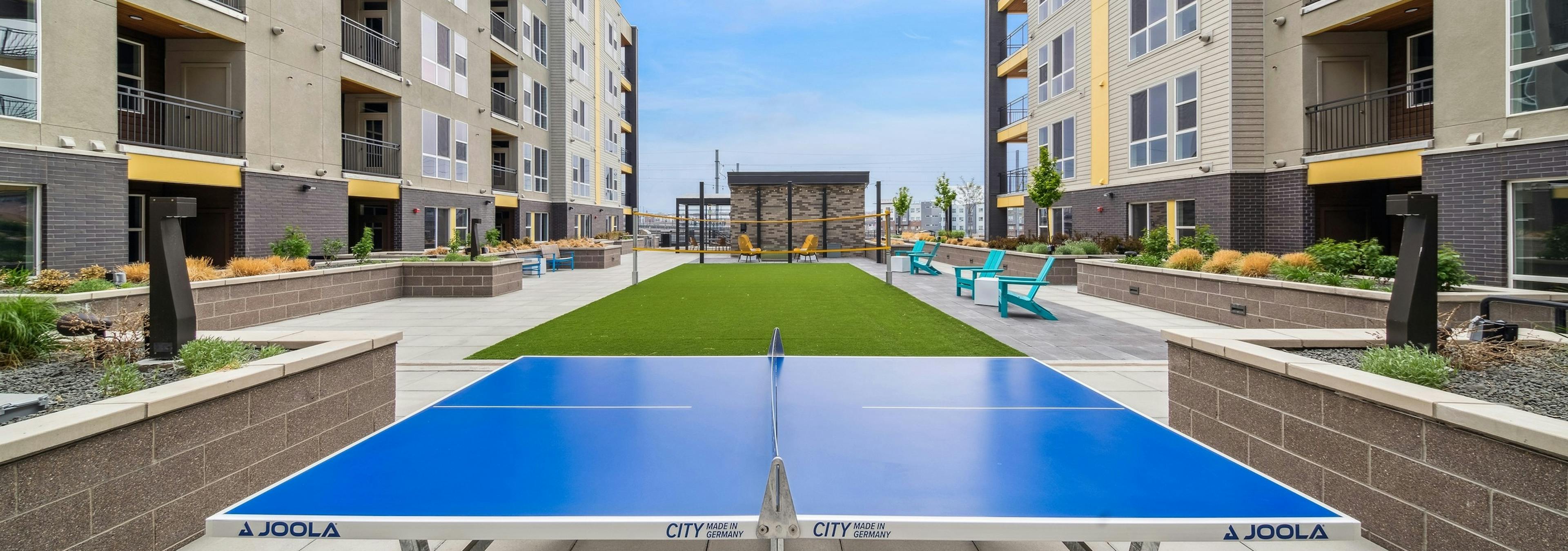 Exterior view of AMLI RiNo courtyard with a blue ping pong table and turf badminton court  surrounded by built-in planters  