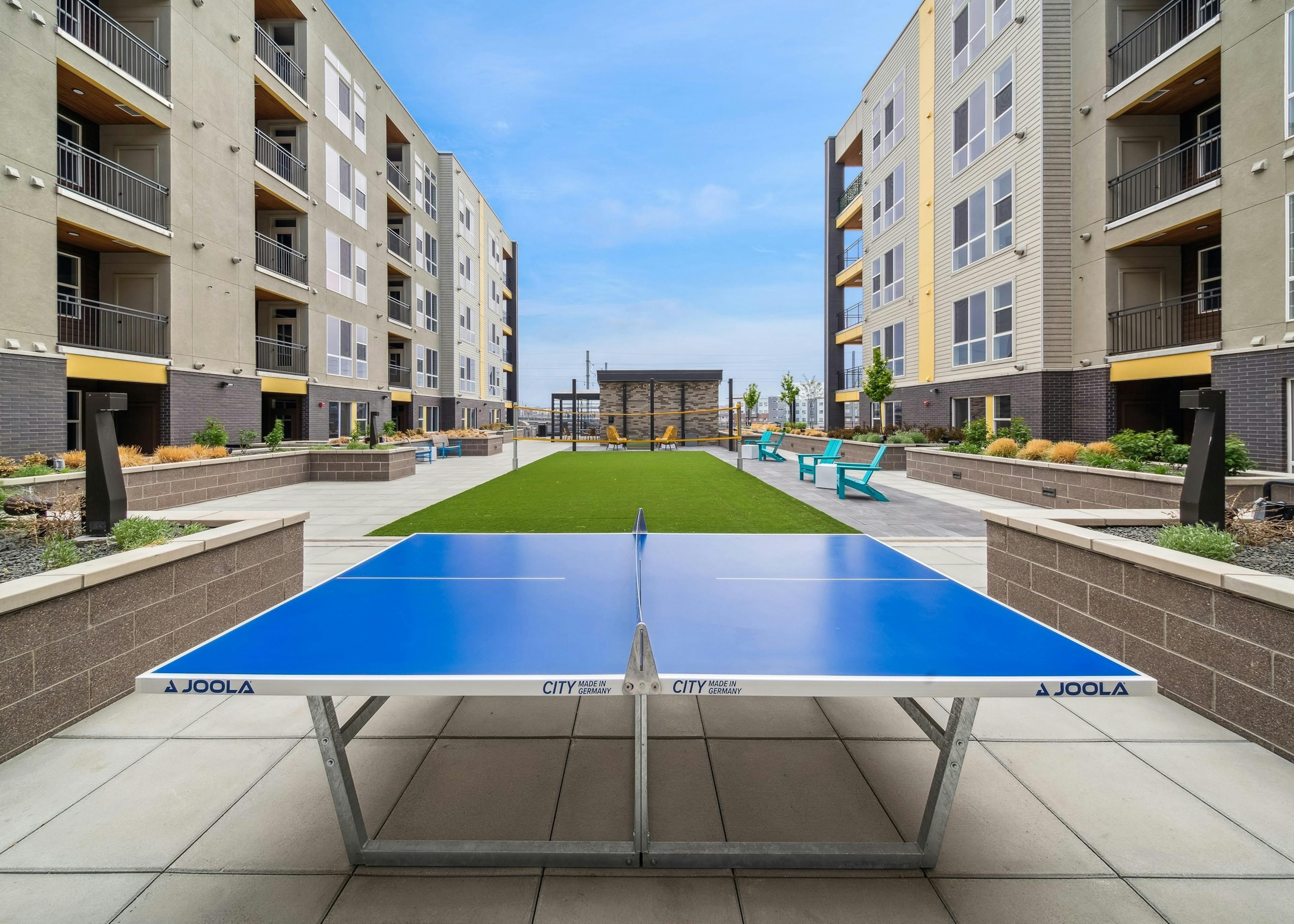 Exterior view of AMLI RiNo courtyard with a blue ping pong table and turf badminton court  surrounded by built-in planters  