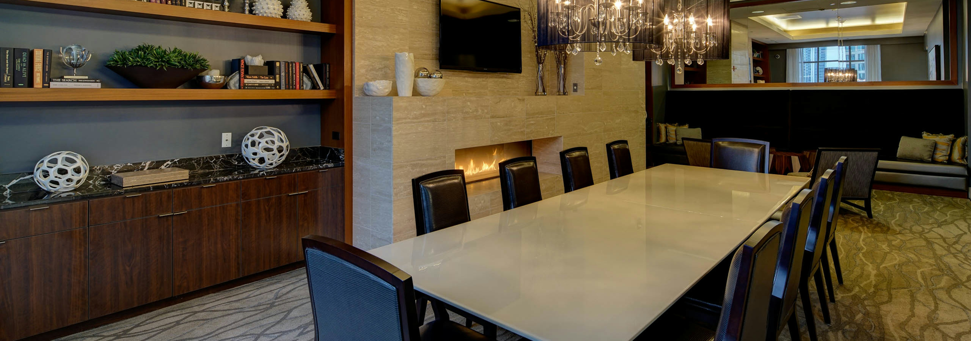 Library at AMLI River North with a long table and black leather chairs and a wooden shelf in the back beside a flat screen TV