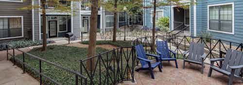 AMLI Eastside courtyard with tall trees and green landscape with black railings and gray and blue chairs set on brick pavers