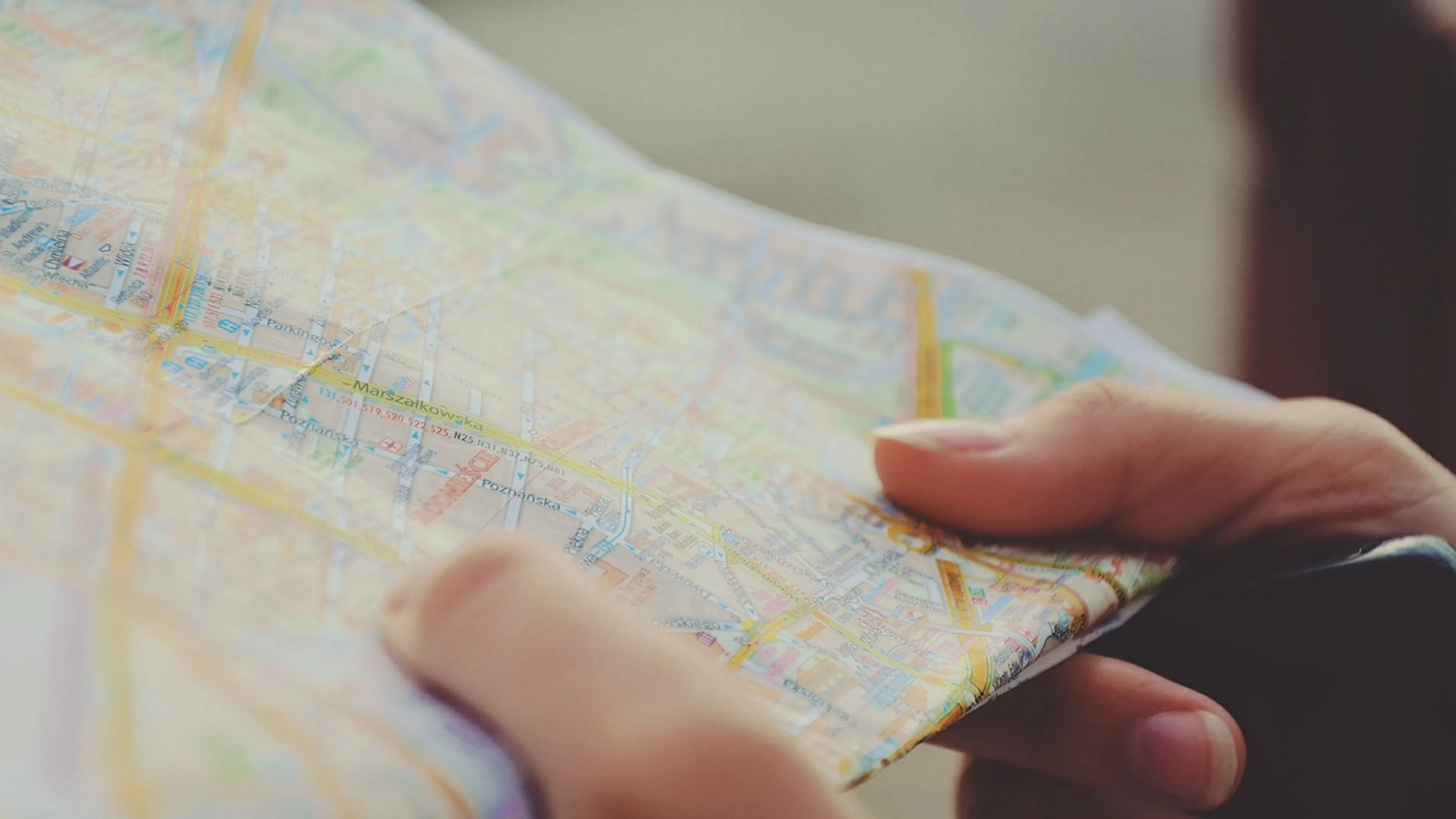 Close up of hands holding a paper road map focusing on city streets and highways with a blurred urban background