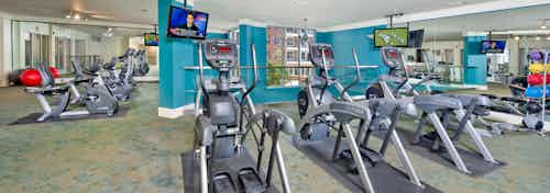 Fitness center at AMLI North Point with blue walls and flat screen TVs above exercise equipment including elliptical machines