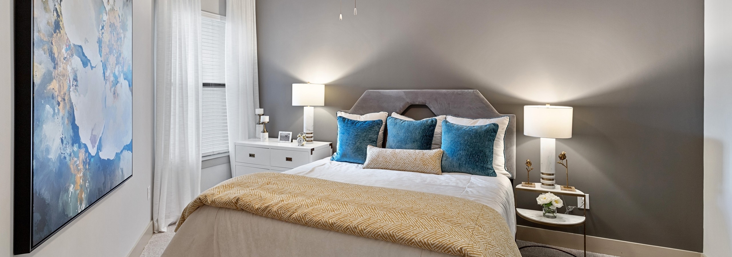 AMLI Parkside apartment bedroom with bed centered on gray wall and nightstands with lamps and a window with white curtains
