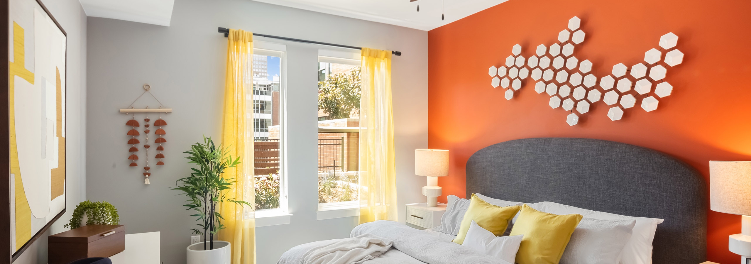 AMLI at Uptown bedroom with a burnt orange accent wall and neutral bedding and decor with pops of yellow throughout the space