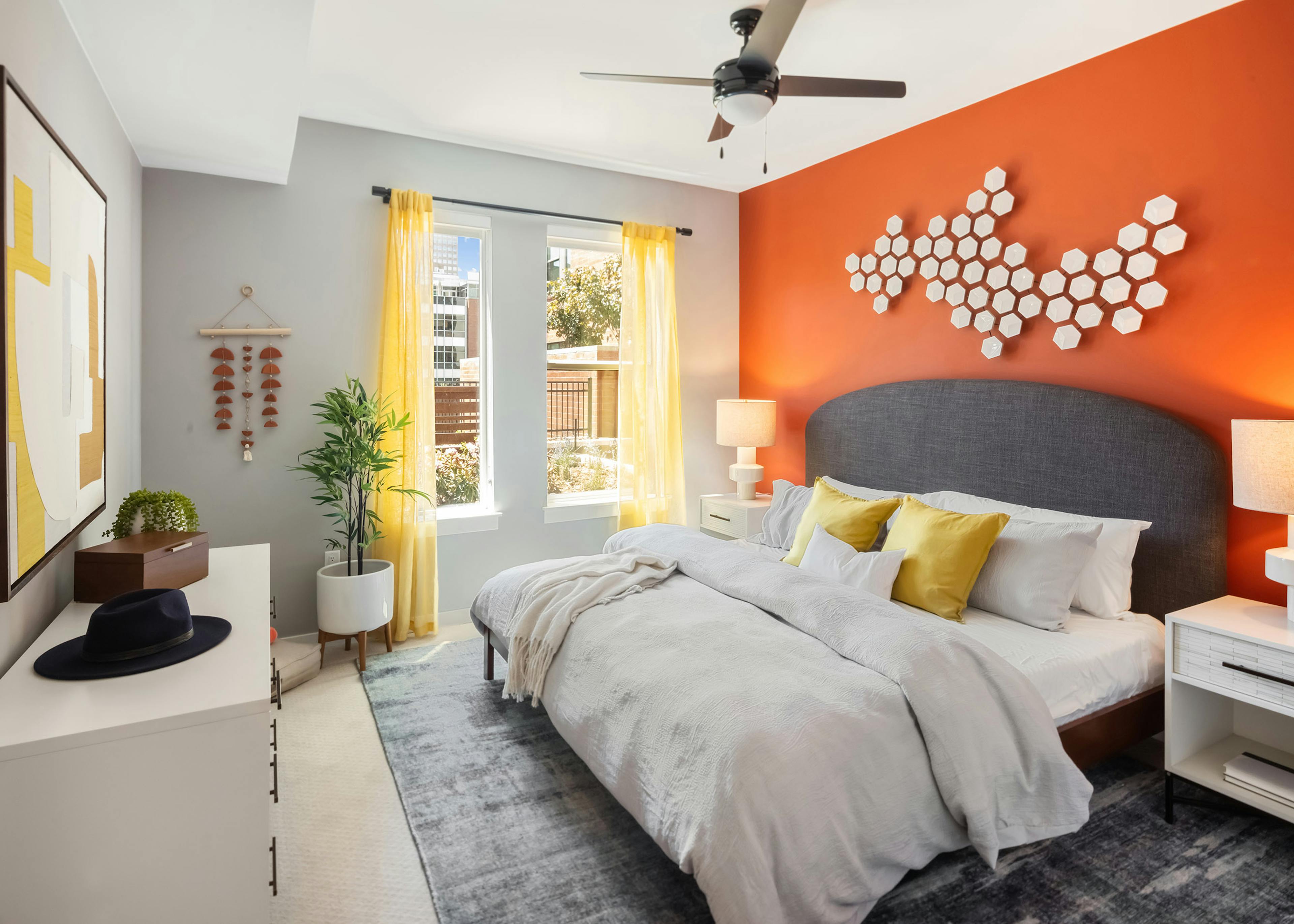 AMLI at Uptown bedroom with a burnt orange accent wall and neutral bedding and decor with pops of yellow throughout the space