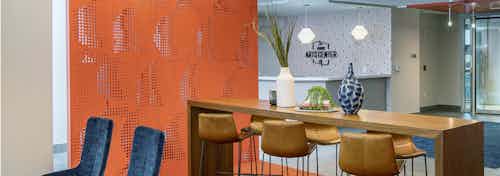 AMLI Arts Center lobby with thin wooden desk and six matching barstools with orange textured wall and modern light fixtures