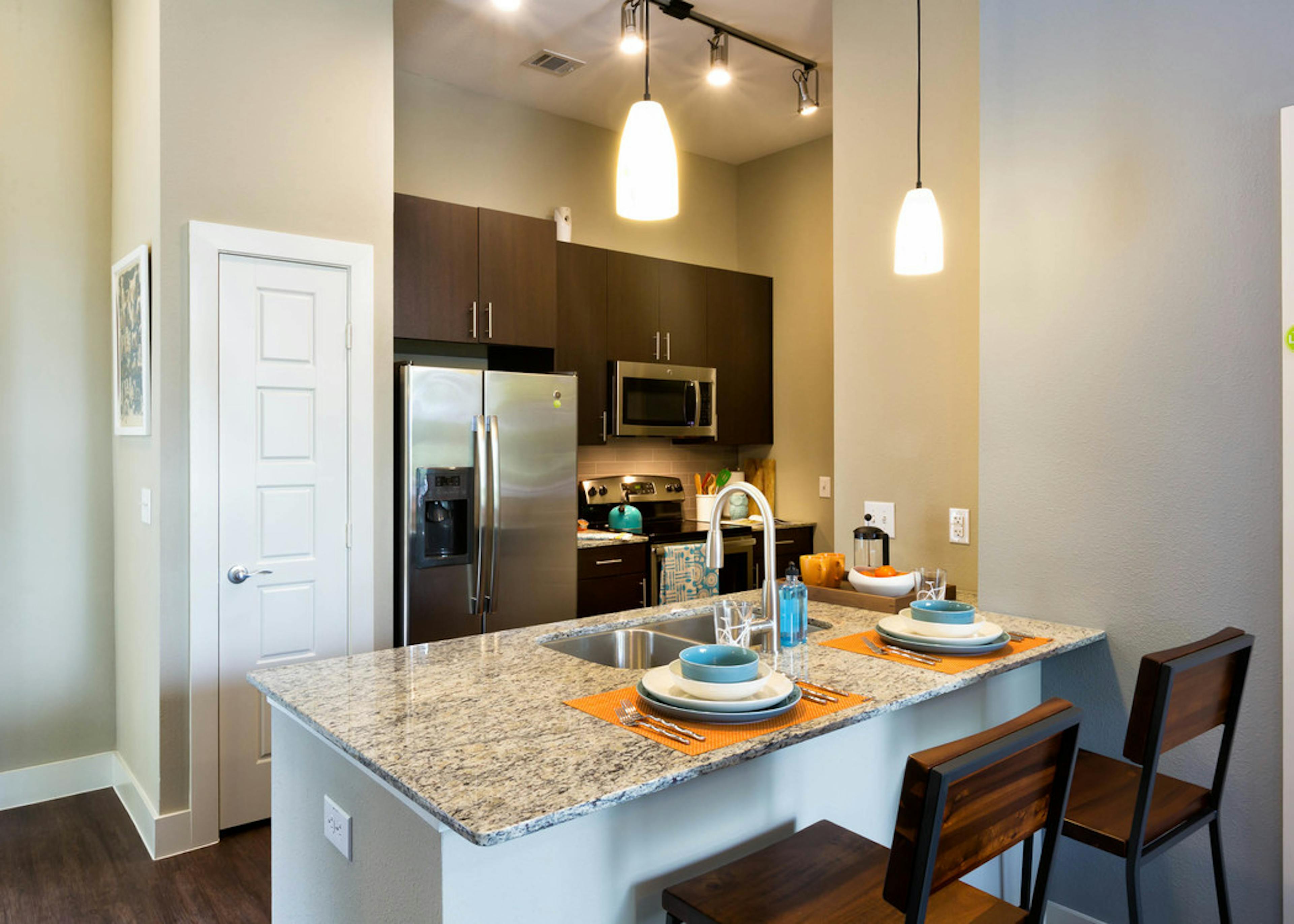 AMLI at Mueller kitchen with stools at a granite counter with dark wood cabinets and stainless steel appliances in background