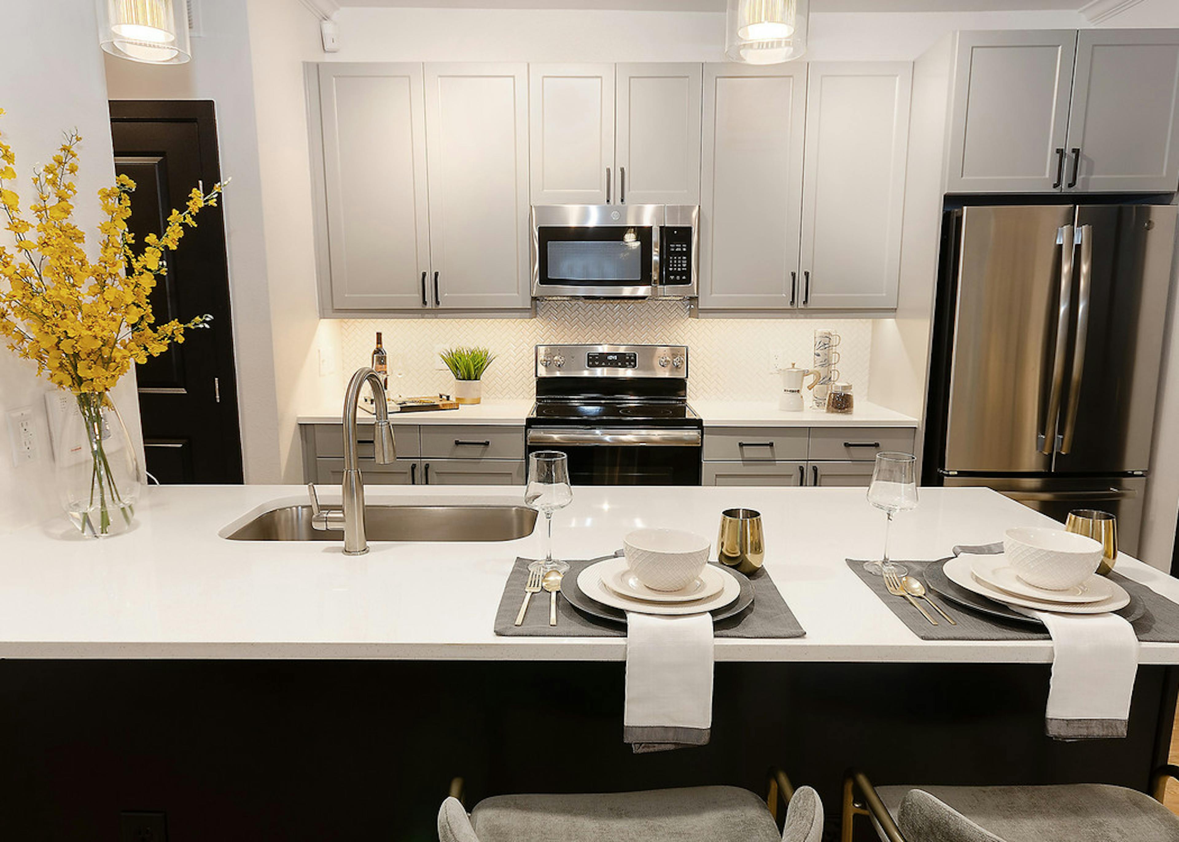 Island kitchen at AMLI Quadrangle with sleek white counters with grey cabinets and stainless steel appliances in background
