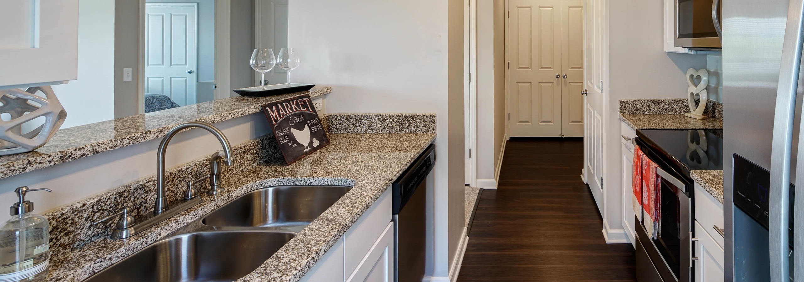 AMLI at Seven Bridges kitchen with white cabinets and granite countertops with dark wood floors leading to a hallway