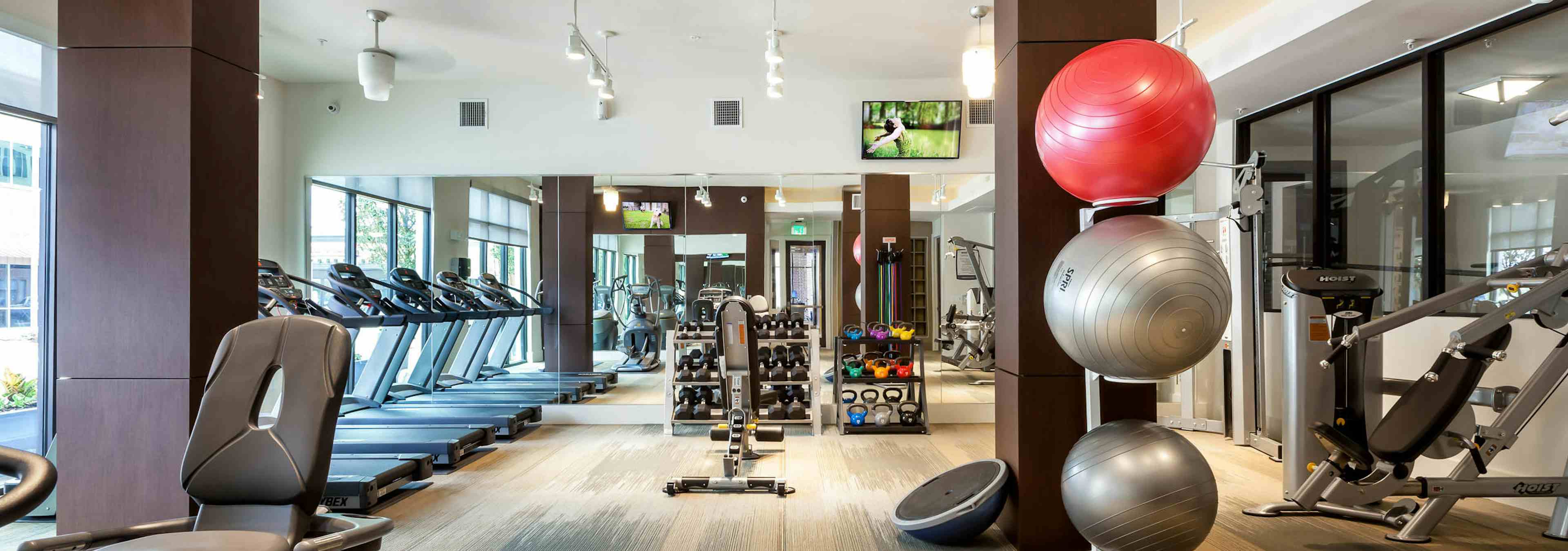 AMLI West Plano fitness center with dark brown pillars and stacked exercise balls with treadmills and dumbbells in background