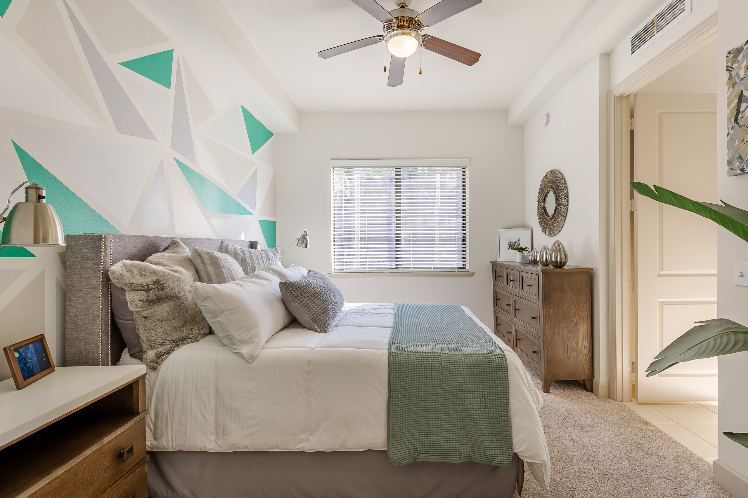 AMLI 880 apartment bedroom with ceiling fan and wood dresser and side table featuring a green and gray geometric wall pattern