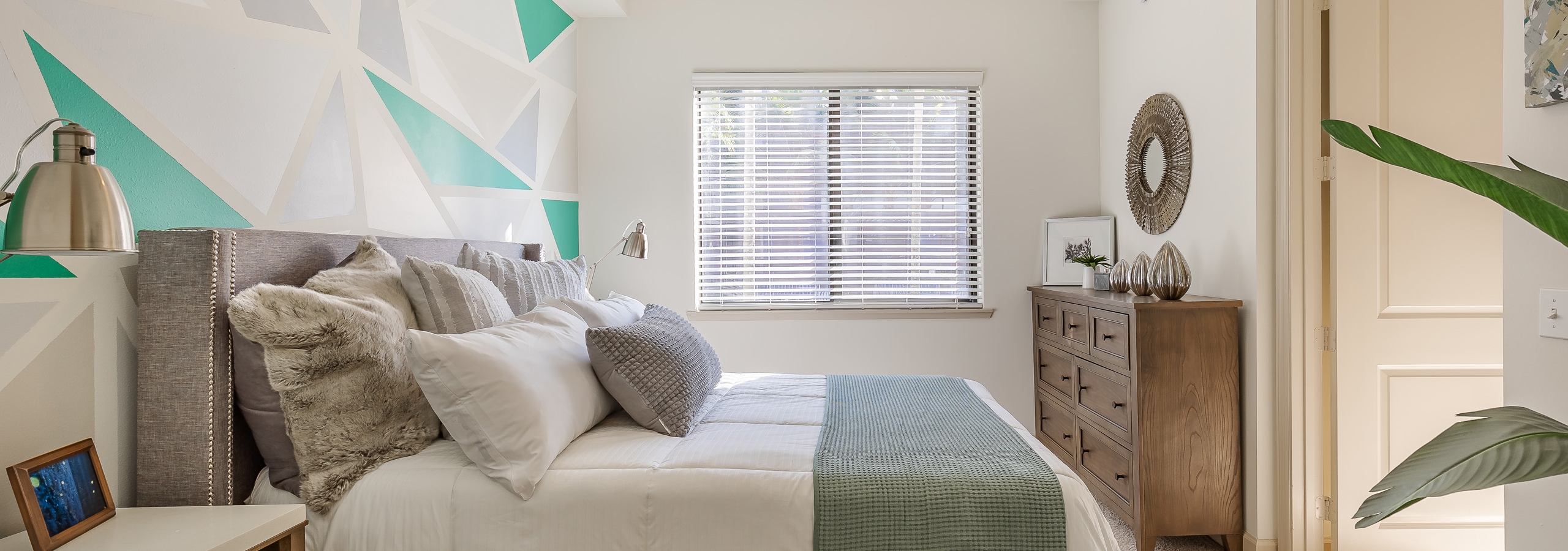 AMLI 880 apartment bedroom with ceiling fan and wood dresser and side table featuring a green and gray geometric wall pattern