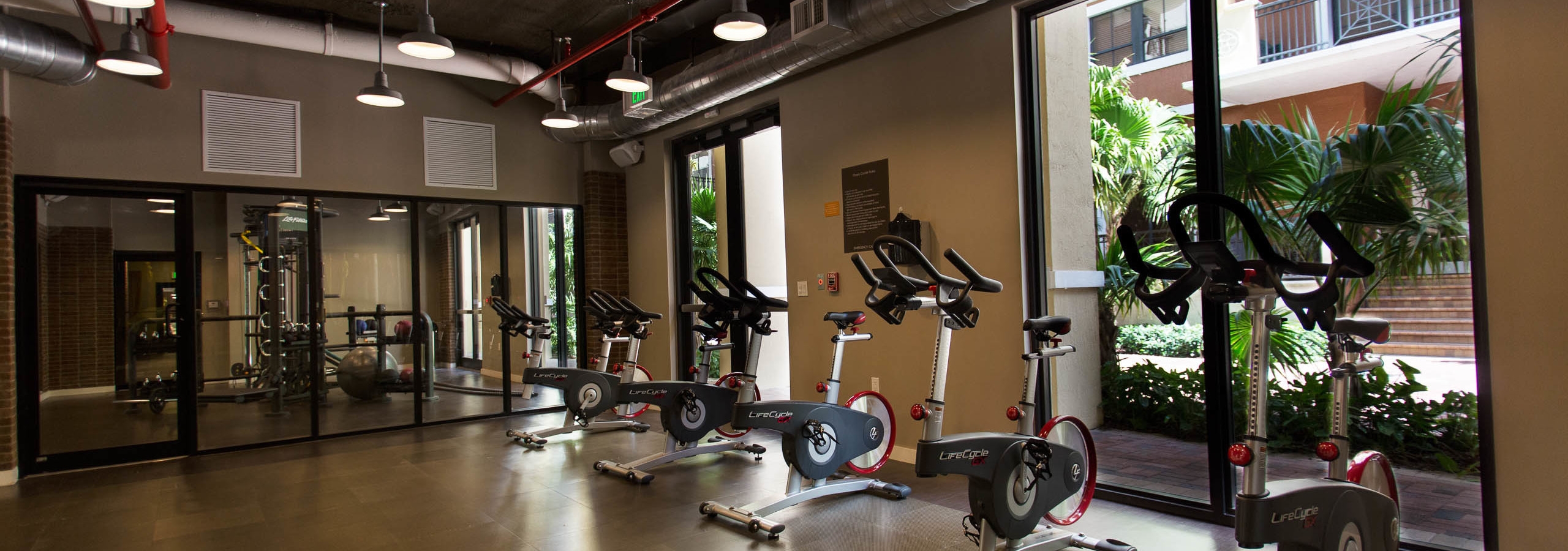 Interior of spinning room at AMLI Dadeland with multiple spin bikes and a view of the  lush landscaped courtyard