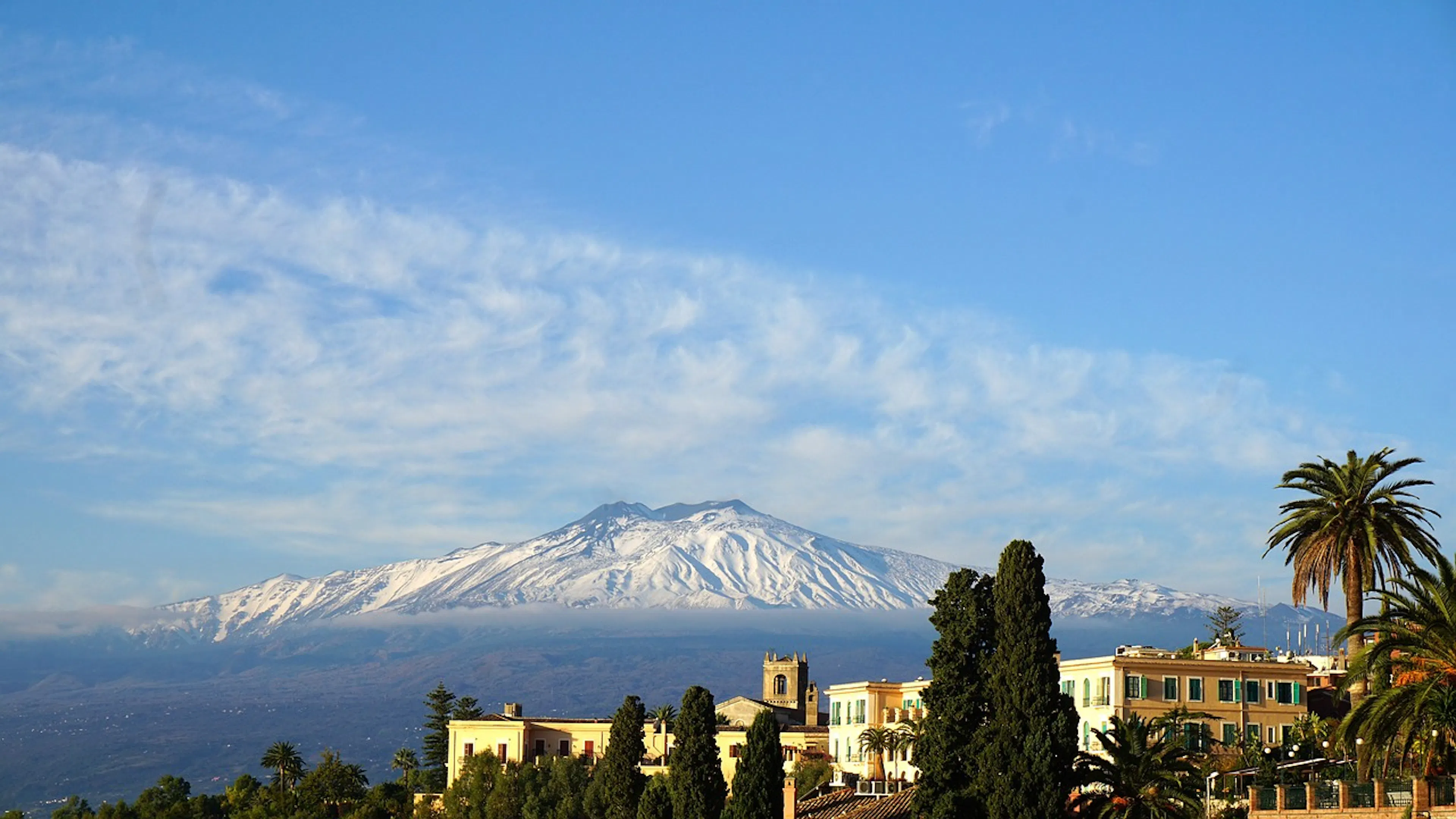 A lanscape view of a tall conical volcano in the distance with a small Mediterranean style town in the foreground