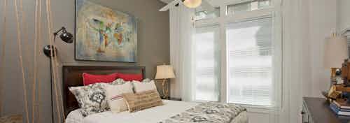 Bedroom at AMLI 5350 with a white bed against a dark grey accent wall next to a large window with sunny daytime views
