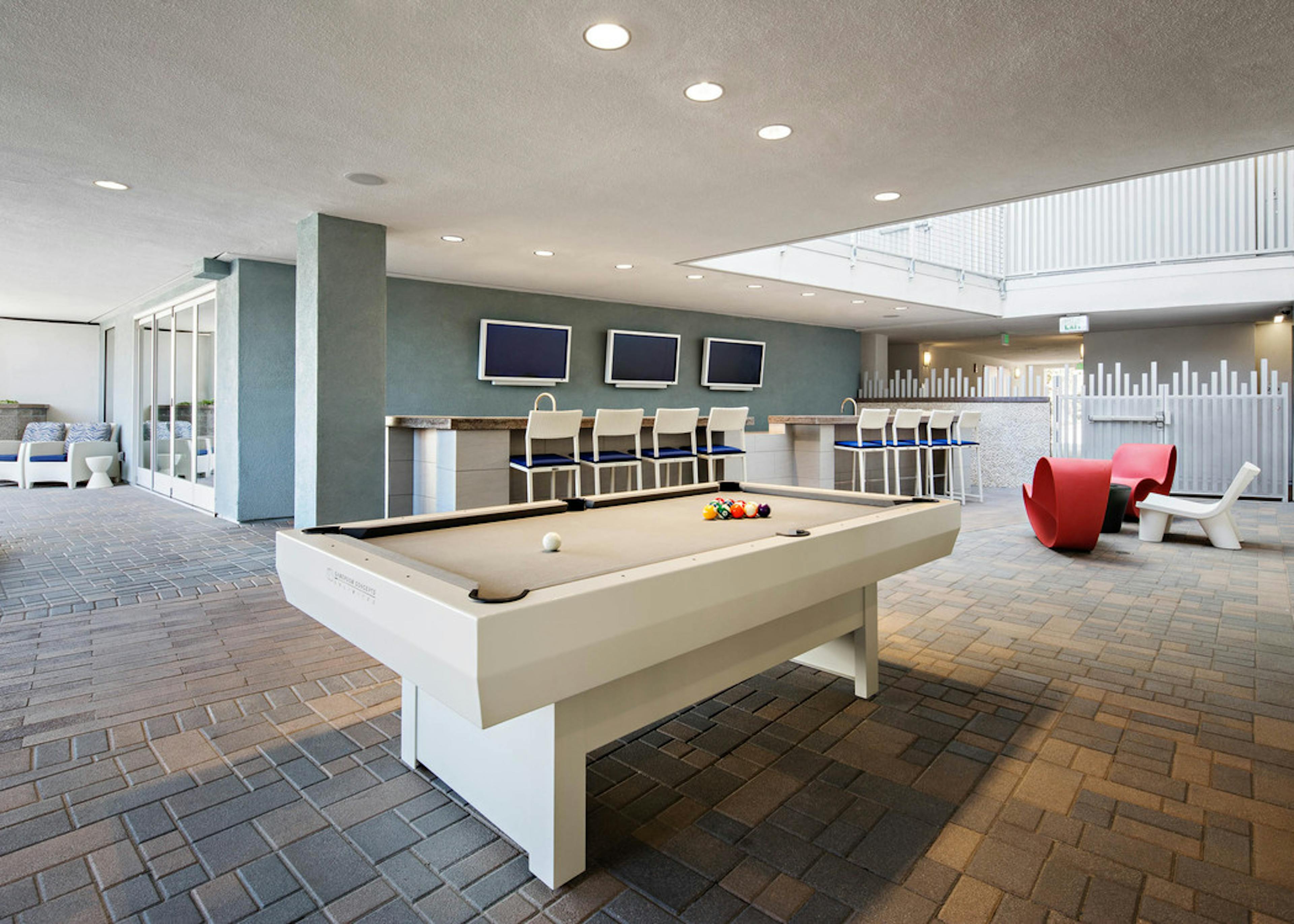 Daytime exterior view of AMLI Lex on Orange outdoor bar and gaming area with white pool table and big screen TVs and seating