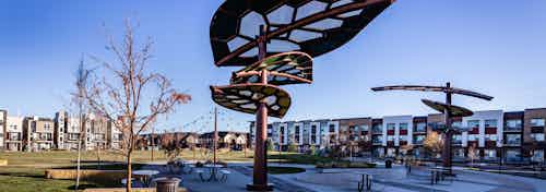Daytime view of AMLI Littleton Village apartment building adjacent to 3.5-acre park with leaf canopies and festoon lighting