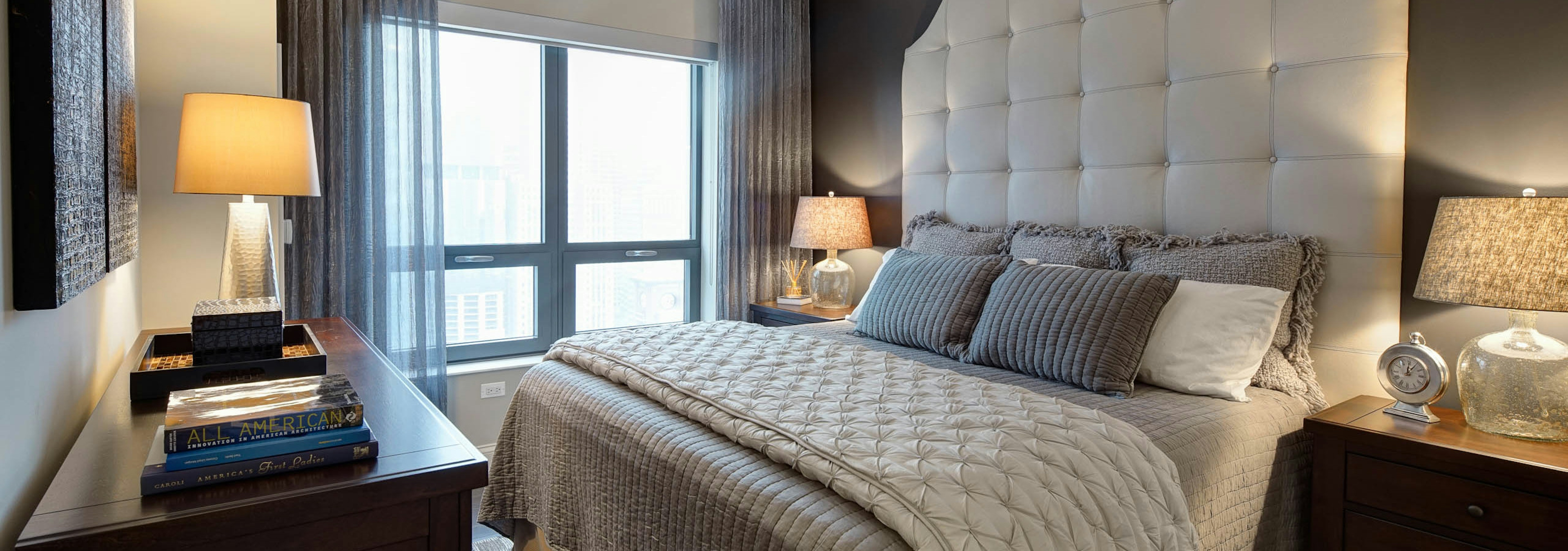 AMLI River North bedroom with natural daytime light and beige decor in front of a window with sheer curtains and a city view