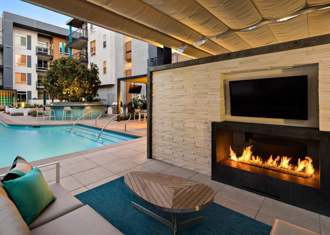 Dusk view of AMLI Uptown Orange outdoor fireplace with individual large screen TV and comfortable seating overlooking pool