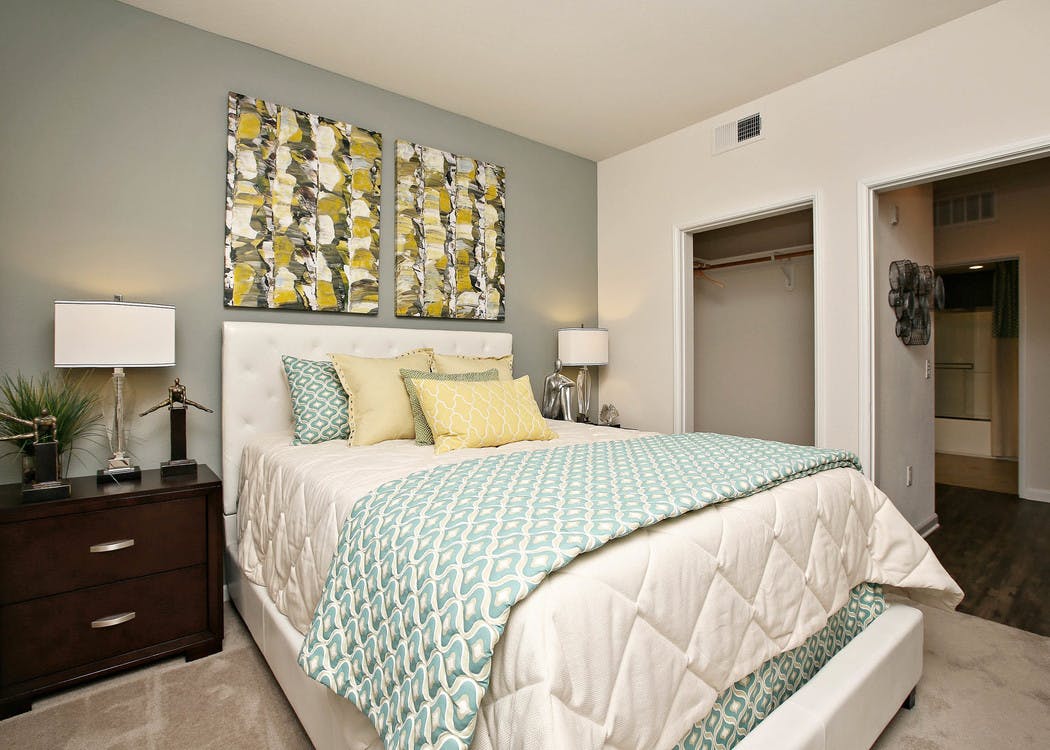 Interior of AMLI Warner Center apartment bedroom with queen size bed with decorative wall art, closet and peek into bathroom