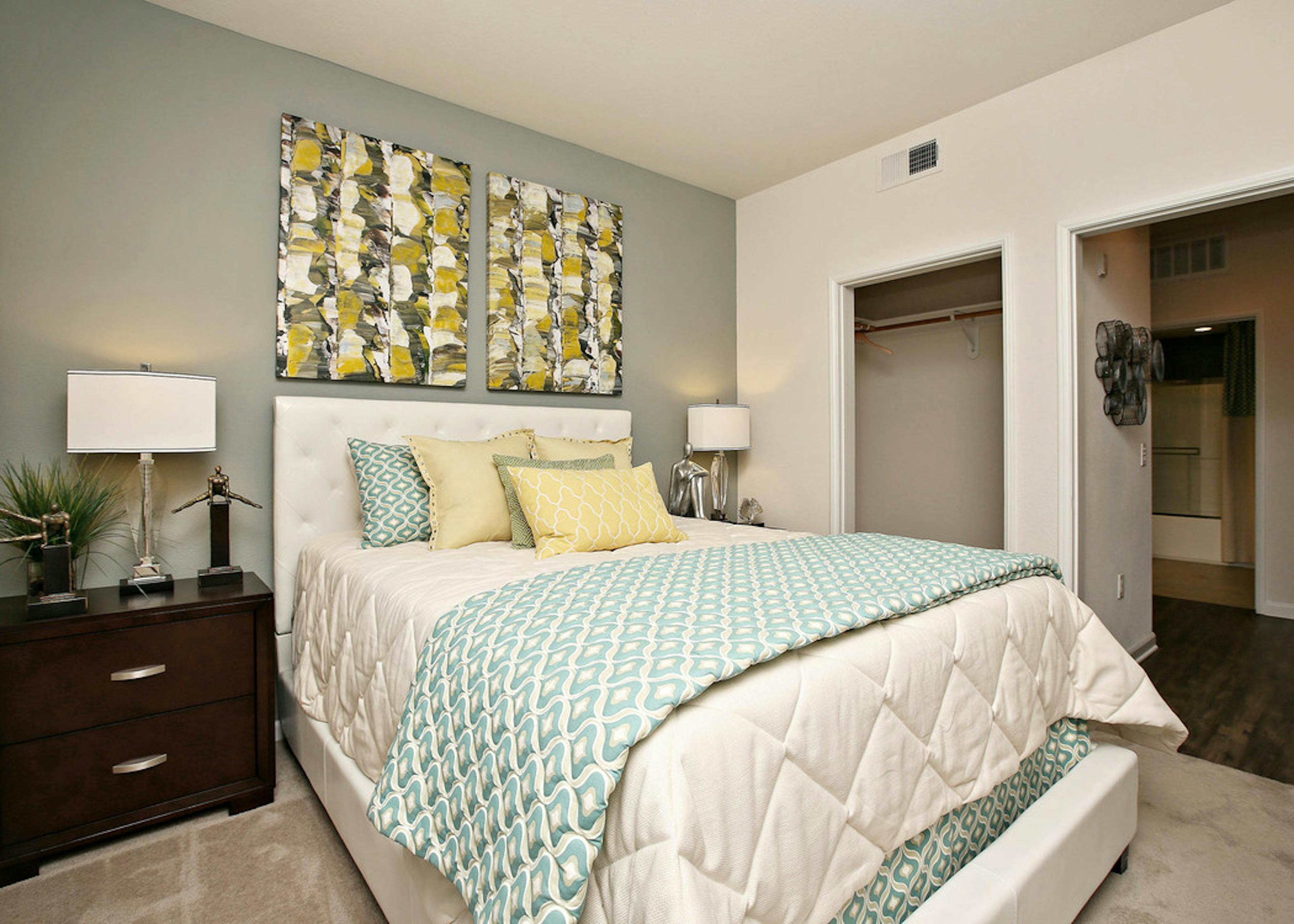 Interior of AMLI Warner Center apartment bedroom with queen size bed with decorative wall art, closet and peek into bathroom