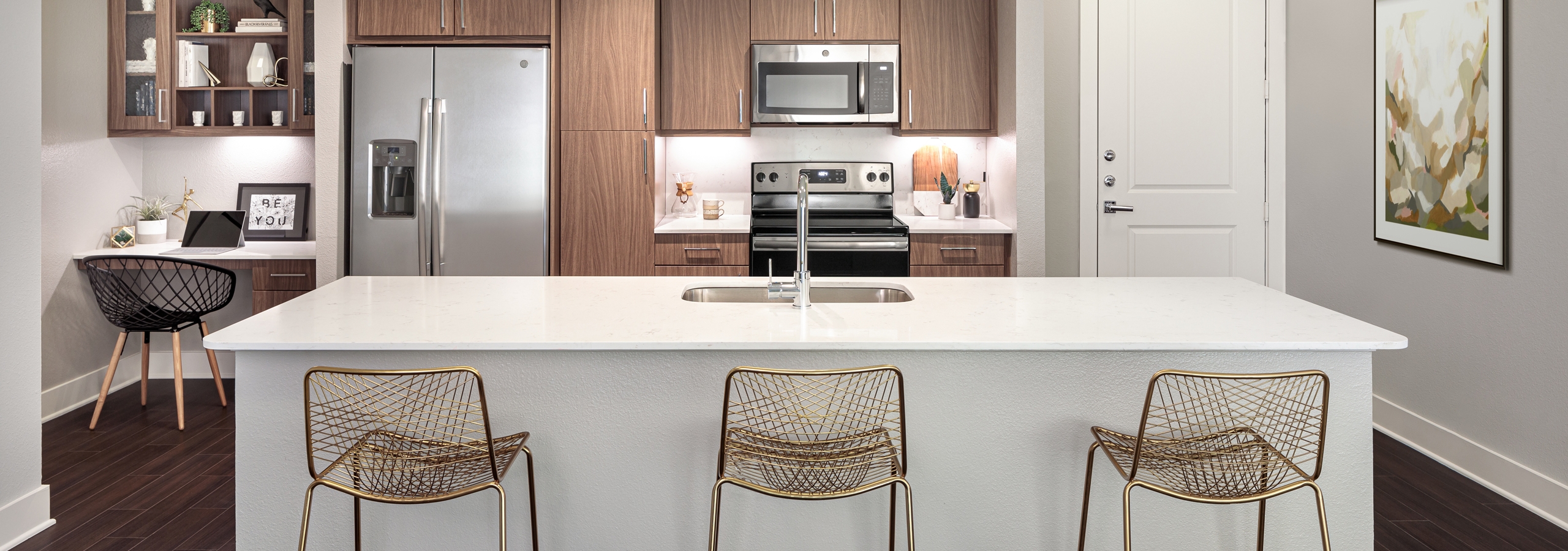 AMLI Addison kitchen with white island and quartz countertops with three barstools and a built in desk next to refrigerator