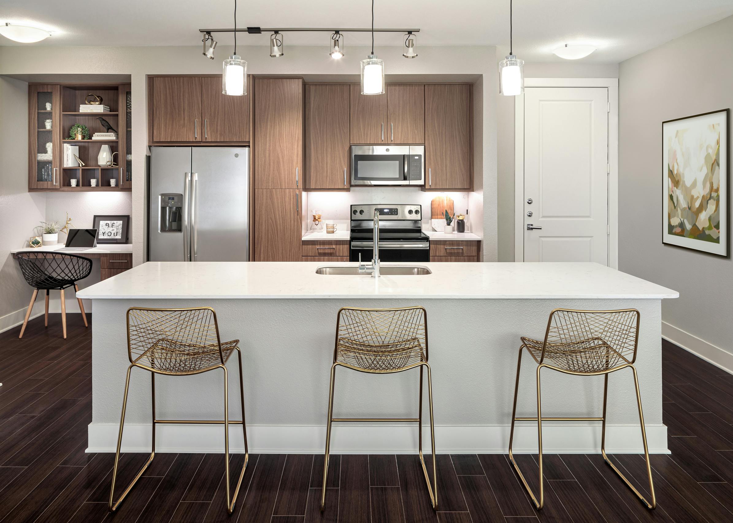 AMLI Addison kitchen with white island and quartz countertops with three barstools and a built in desk next to refrigerator