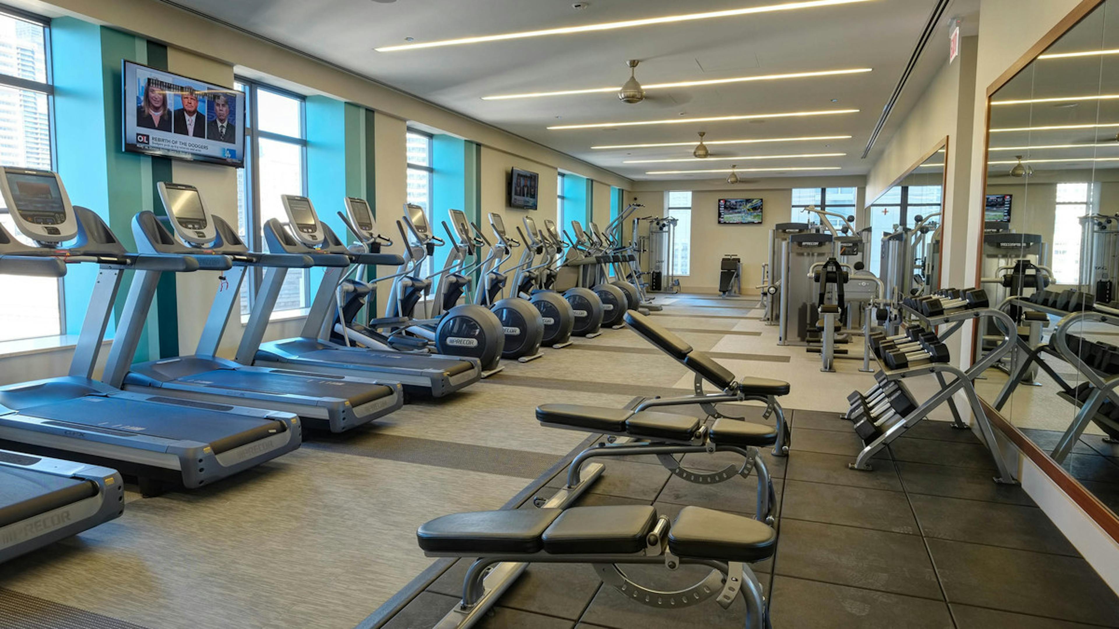 Fitness center at AMLI River North with TVs hanging above treadmills and dumbbells on a shelf near a large wall mirror