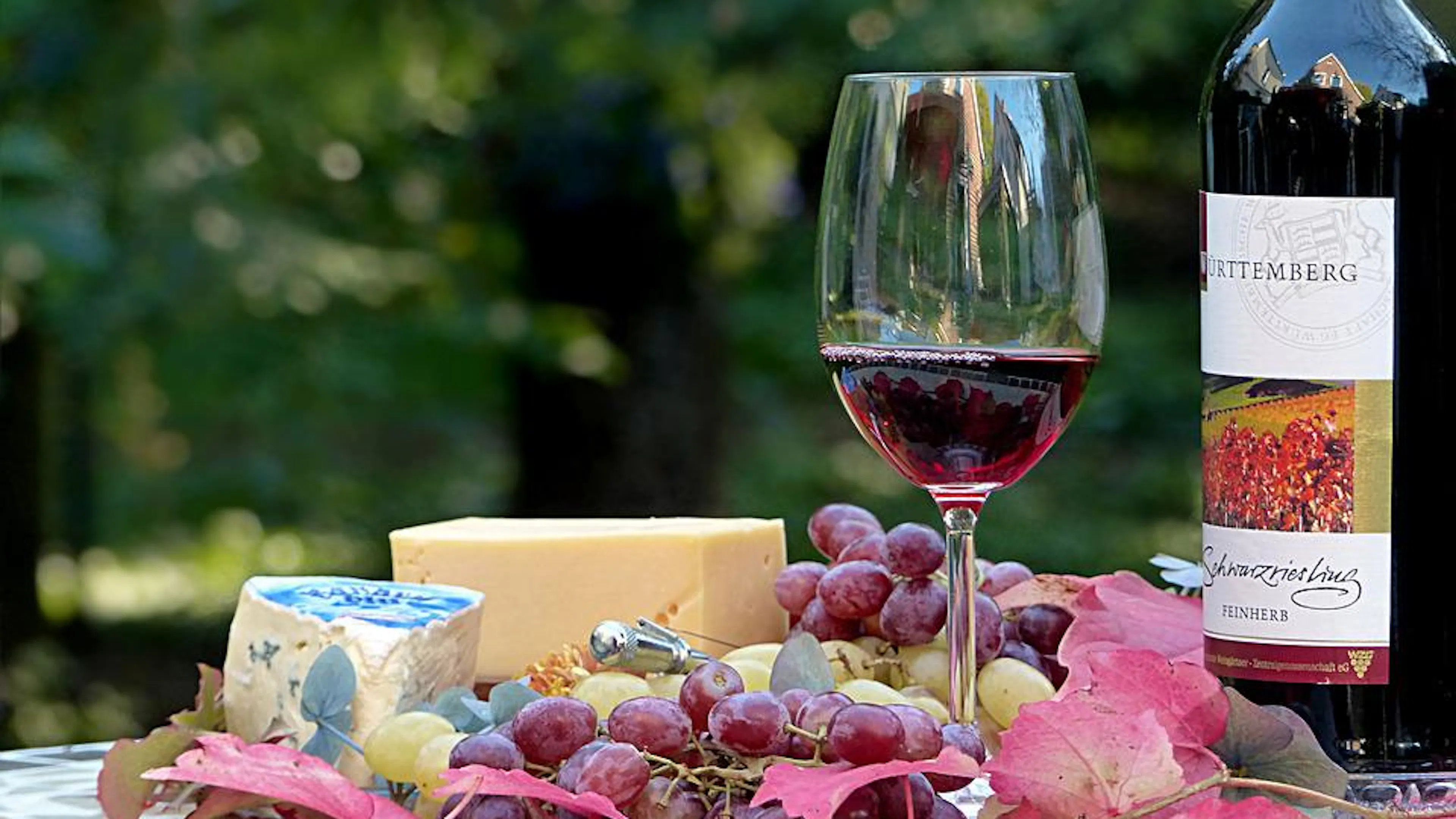  A glass of red wine next to a wine bottle and some cheese and grapes