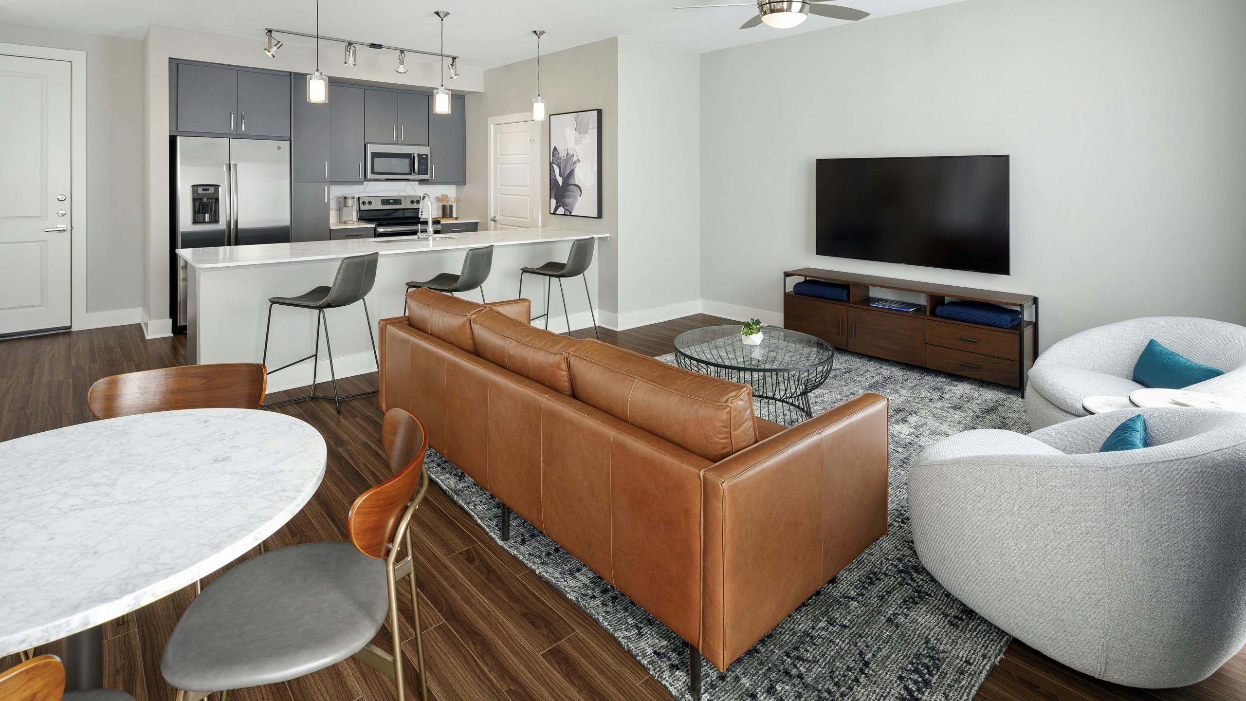 Apartment living area at AMLI Addison with brown plank floor and kitchen with white quartz countertop and stainless appliances