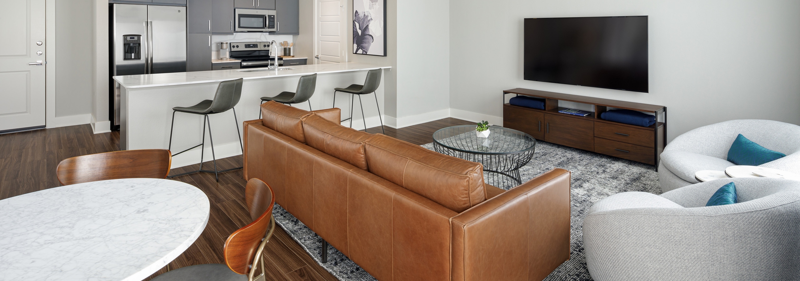 Apartment living area at AMLI Addison with brown plank floor and kitchen with white quartz countertop and stainless appliances