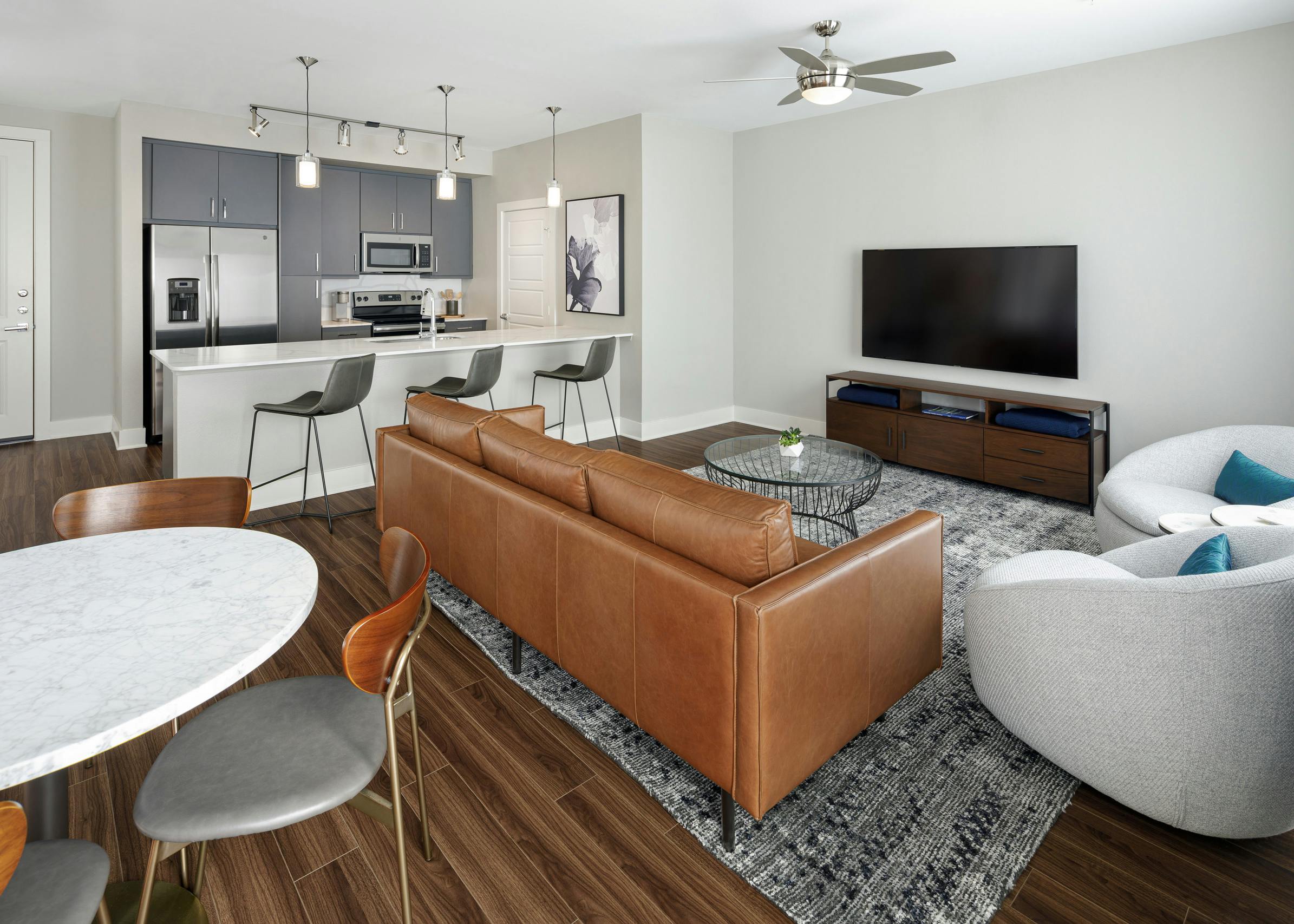 Apartment living area at AMLI Addison with brown plank floor and kitchen with white quartz countertop and stainless appliances