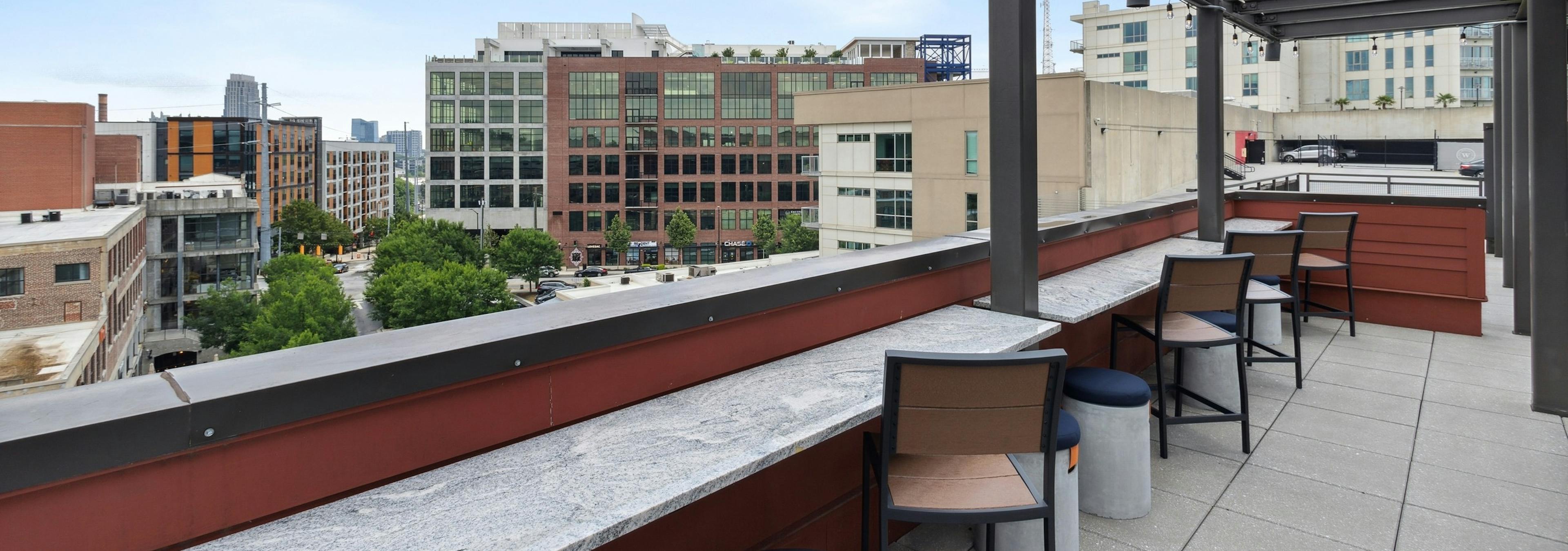 Rooftop lounge side bar with hanging lights and wooden chairs with Midtown skyline views at AMLI Westside apartments
