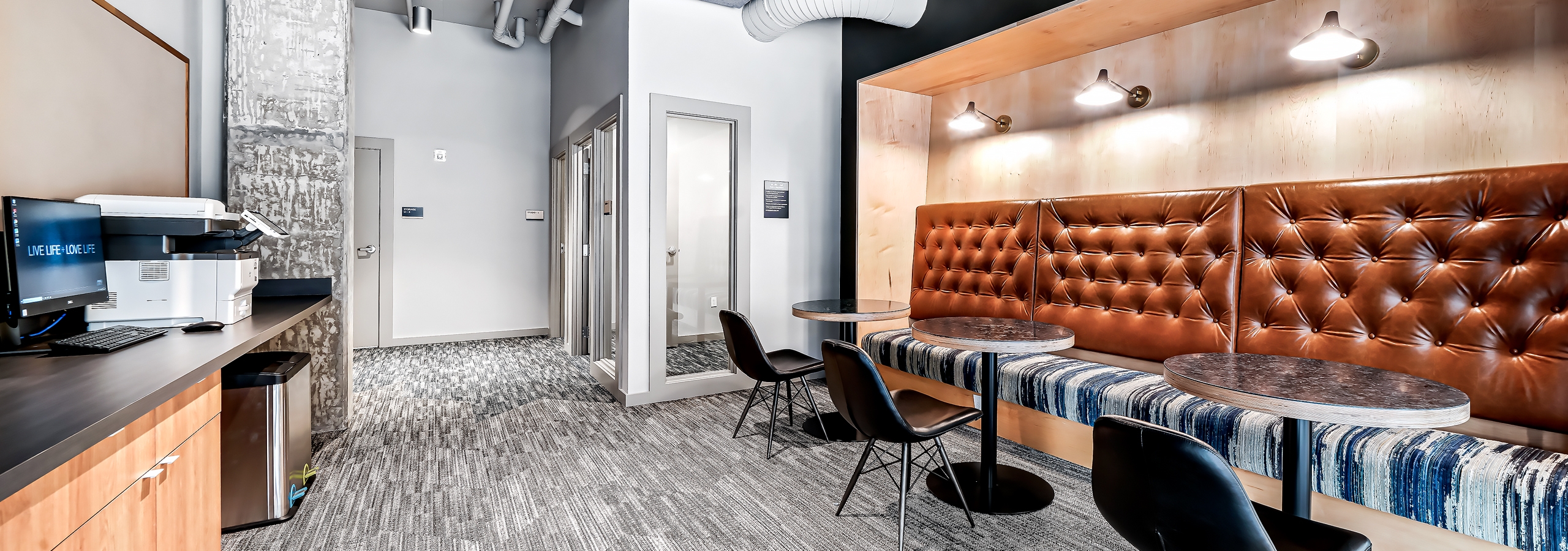 Coworking space at AMLI Spring District apartments with private offices and brown booth with tables and computer and printer