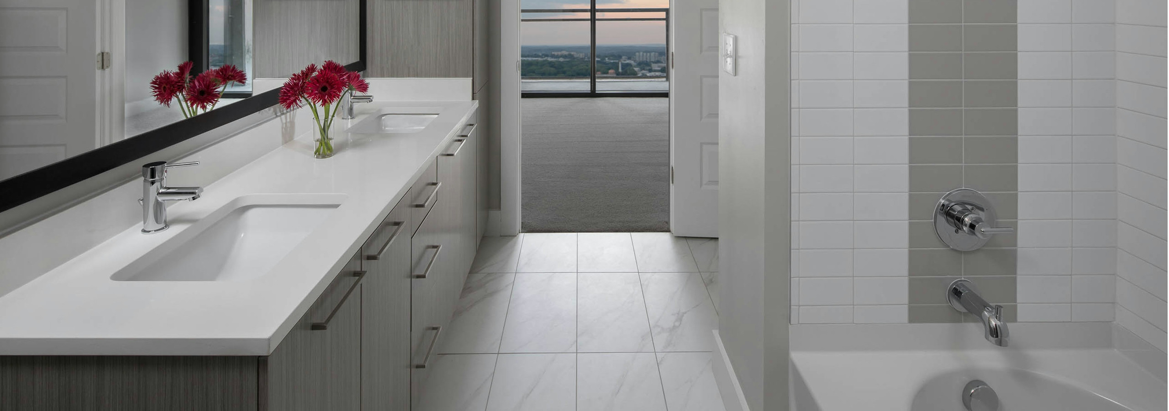 Interior of bathroom at AMLI Arts Center with double vanity sink and white tile flooring with a grey and white tiled bathtub