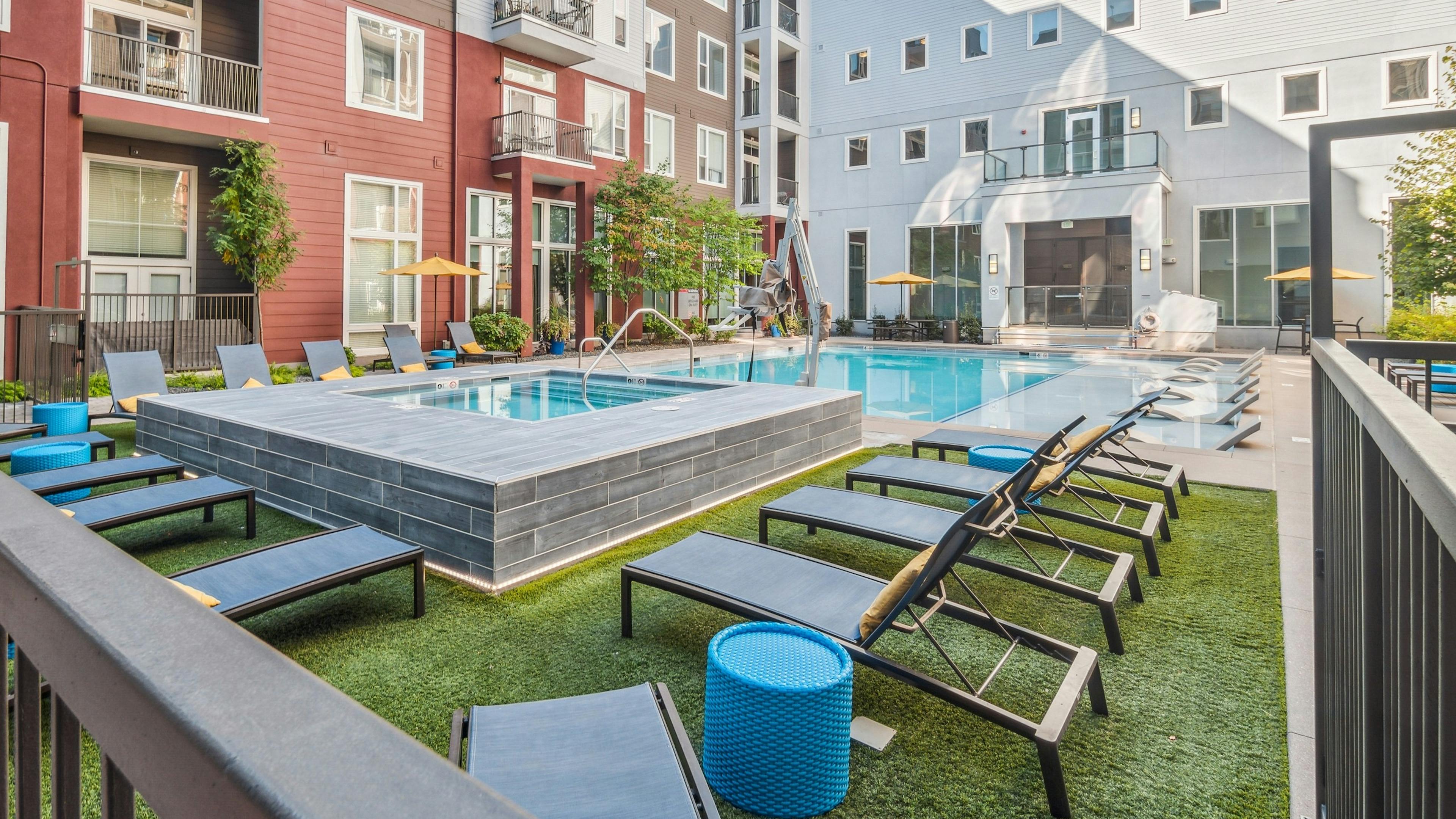 Exterior view of the pool area at AMLI Denargo Market with a hot tub and lounge chairs on turf with building in background