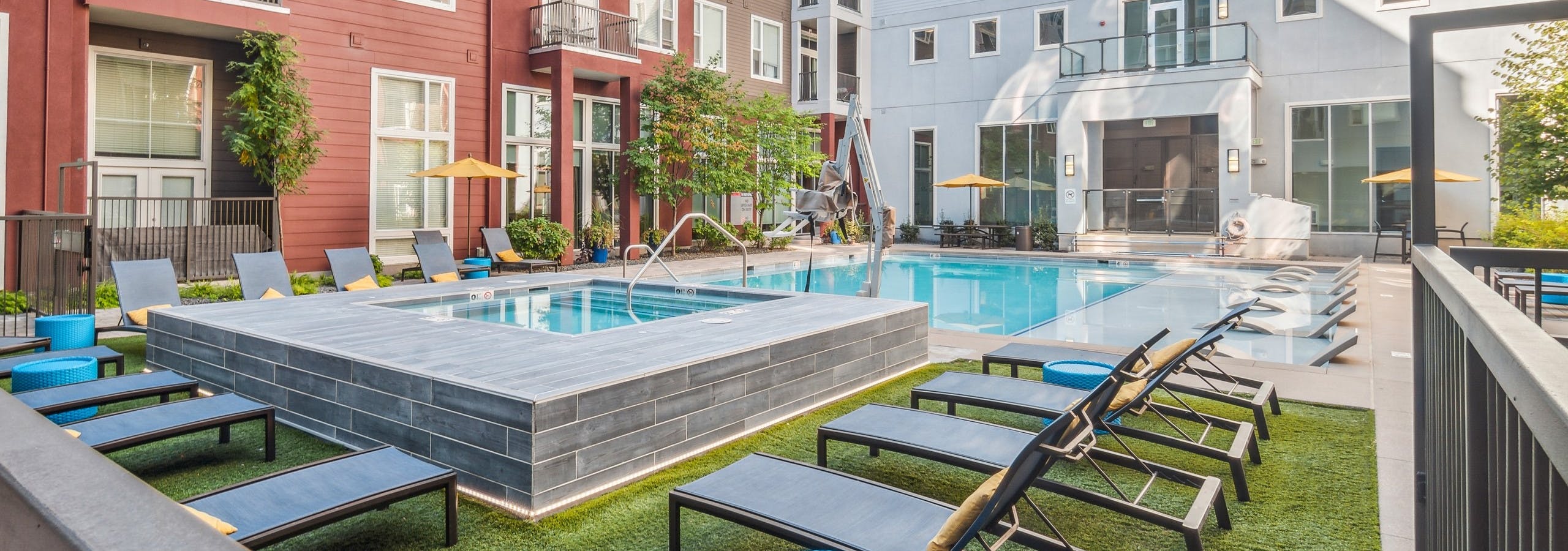 Exterior view of the pool area at AMLI Denargo Market with a hot tub and lounge chairs on turf with building in background