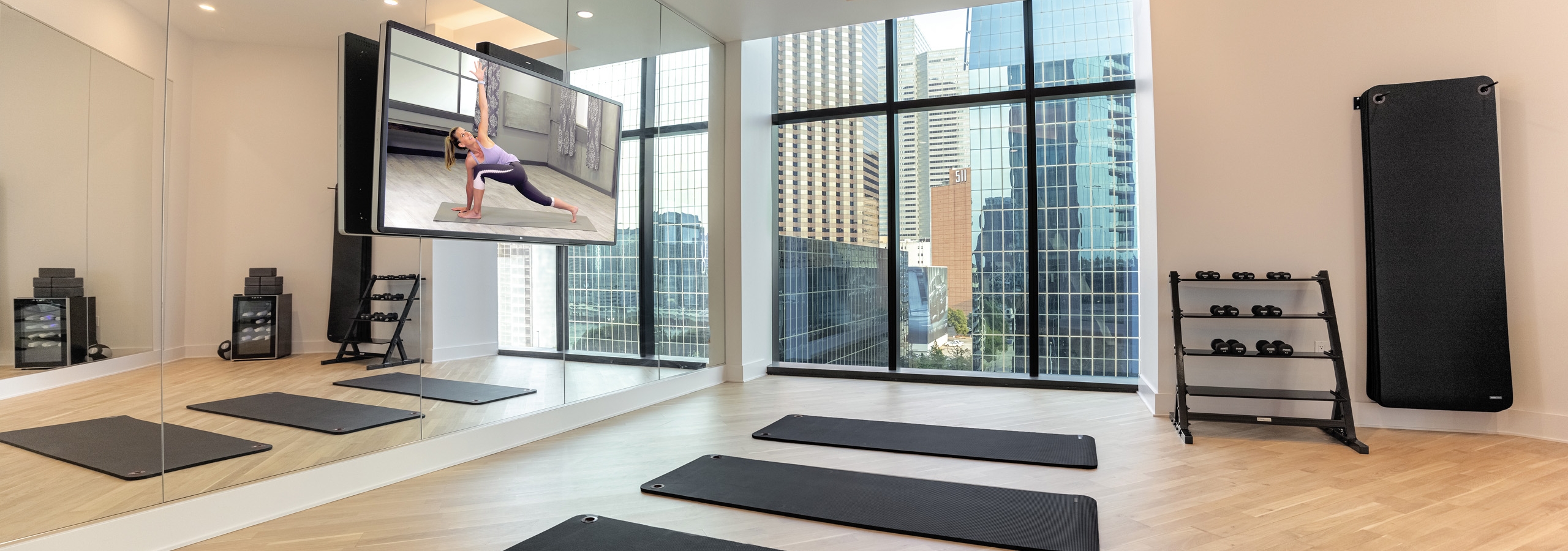 AMLI Fountain Place apartment building yoga room with mirrored wall with large screen TV and wood floors with 3 black mats.