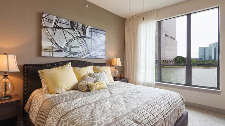 Interior view of AMLI Las Colinas apartment bedroom with bed and nightstands and large window with curtains overlooking lake
