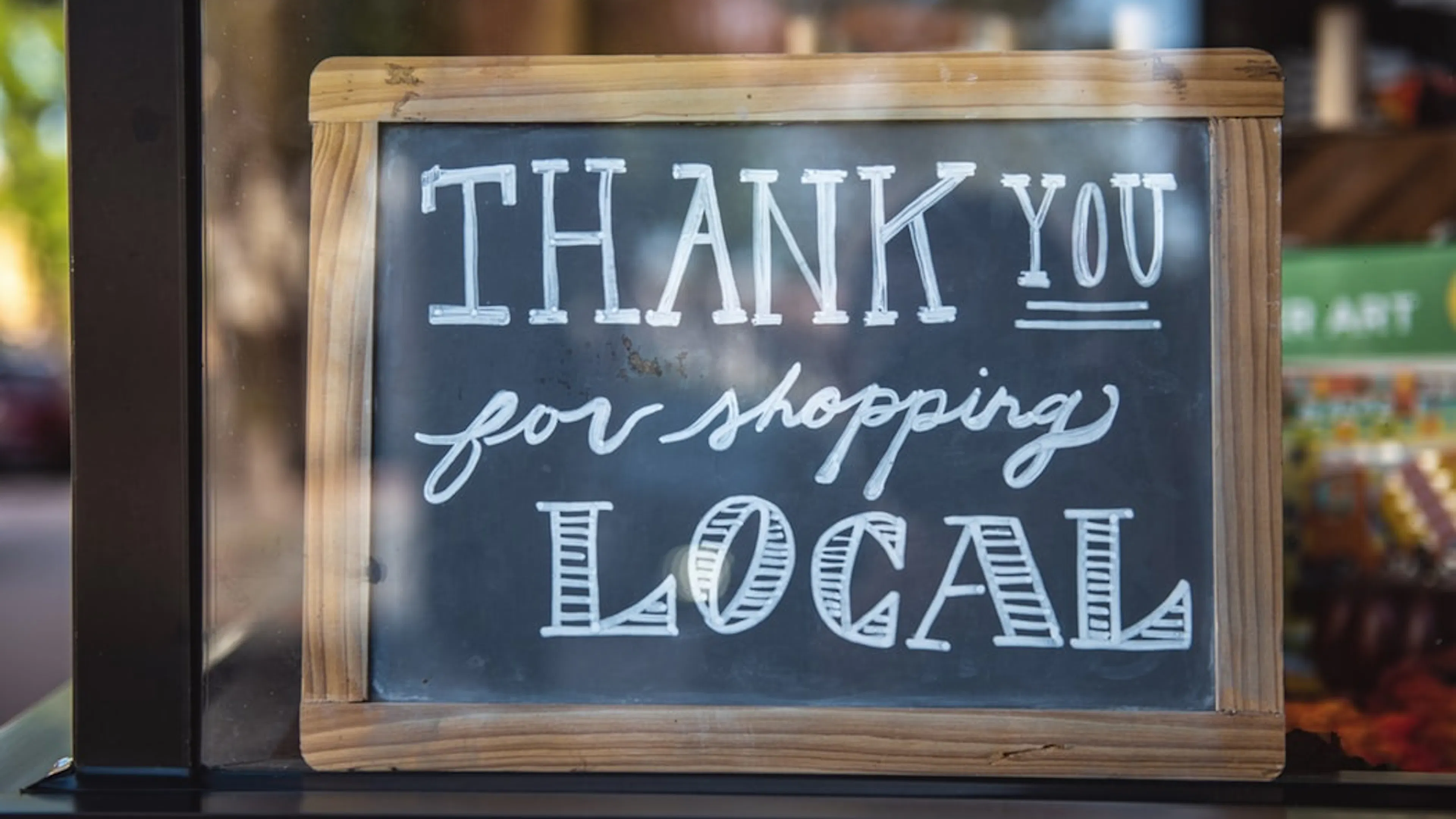Small chalkboard sign saying thank you for shopping local in the window of small business storefront