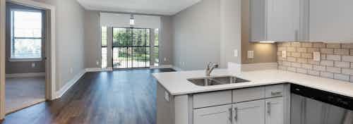 Kitchen at AMLI Eastside with light grey cabinets and quartz countertops with view of open living space and peek into bedroom