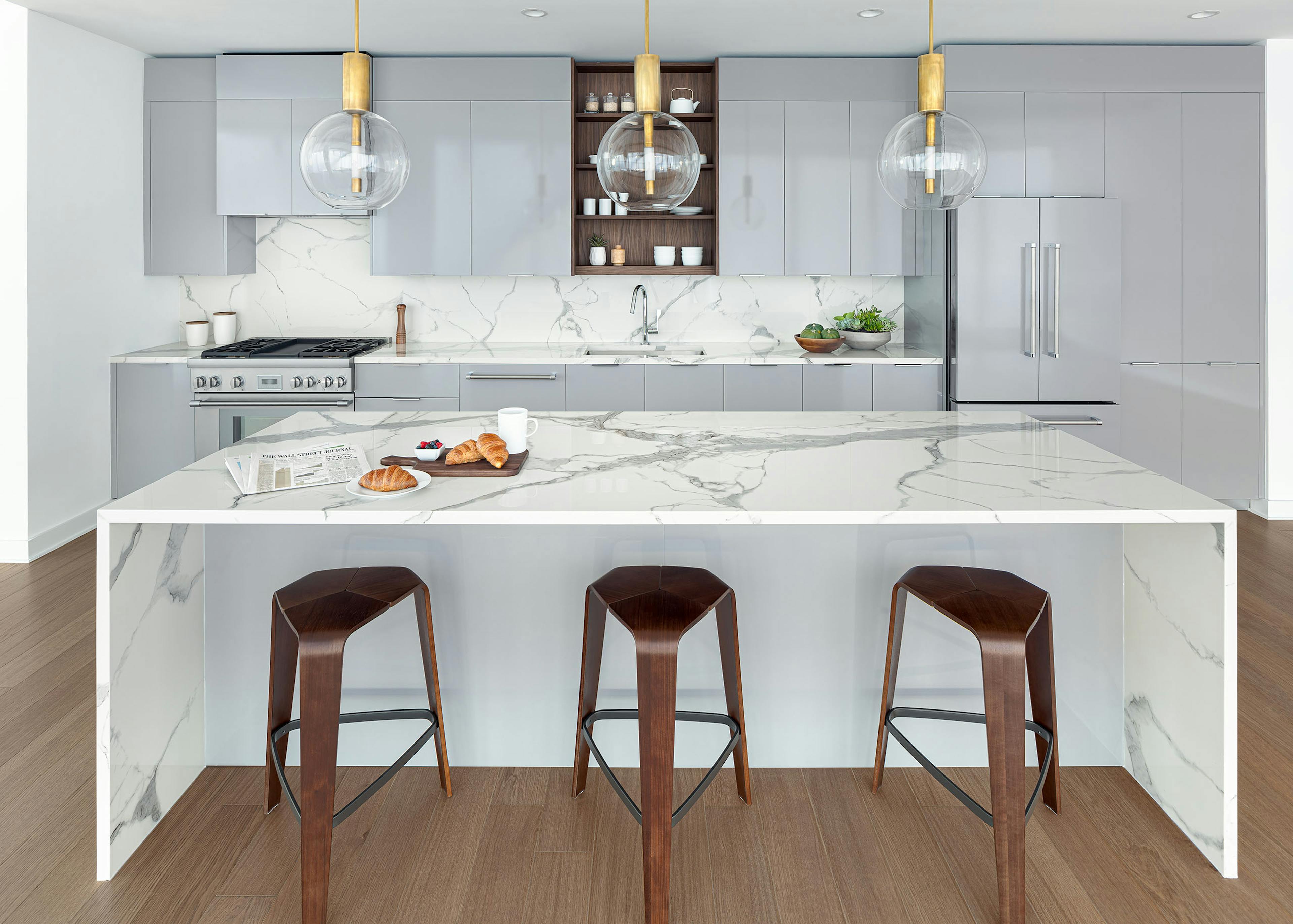 AMLI Fountain Place penthouse kitchen with gray cabinets and a white stone island with glass and gold pendant lights above 