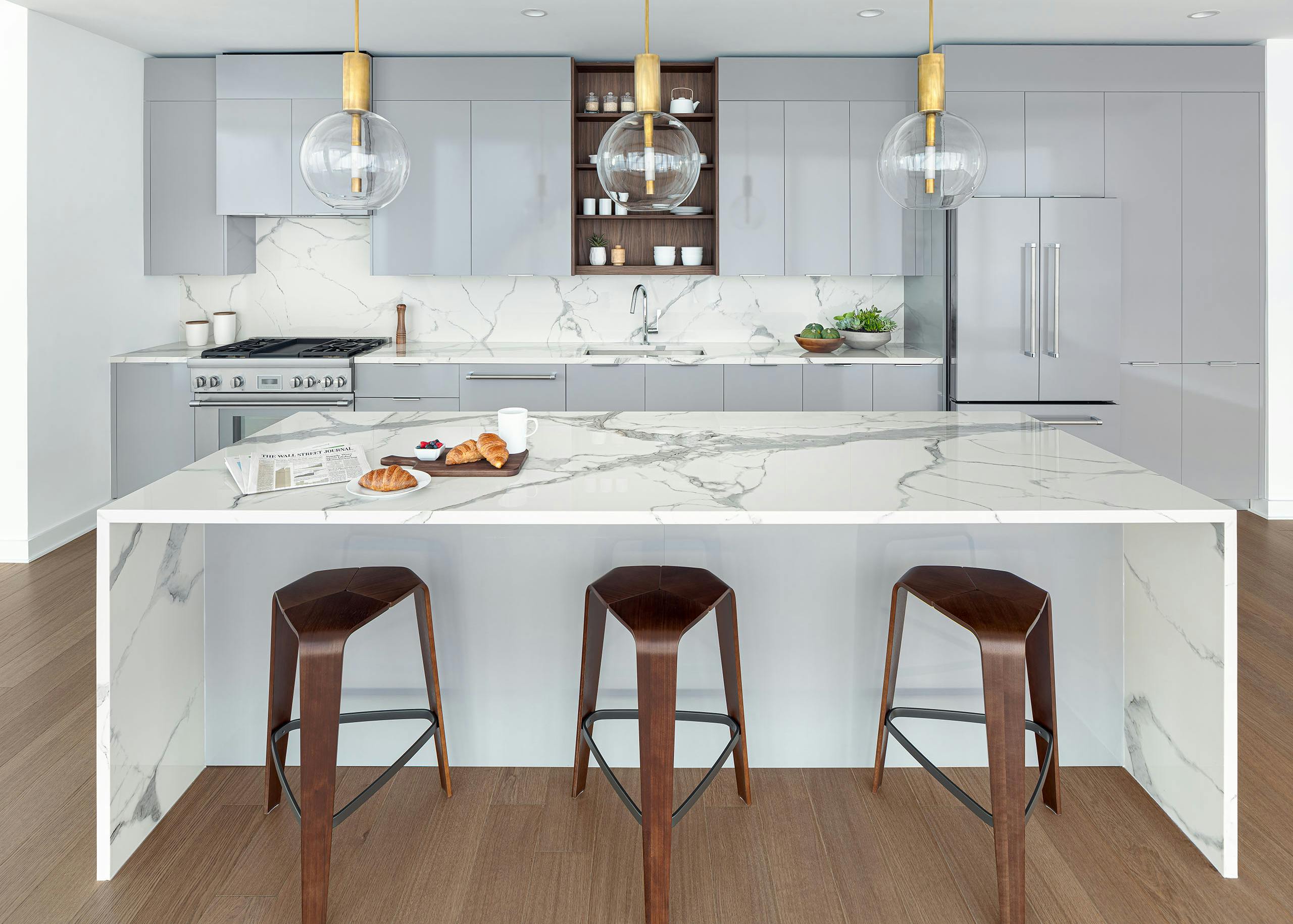AMLI Fountain Place penthouse kitchen with gray cabinets and a white stone island with glass and gold pendant lights above