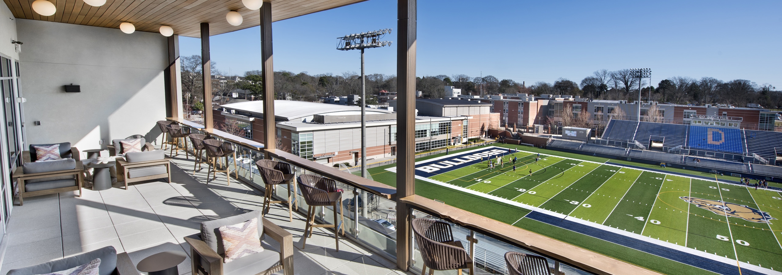 Daytime view of sky lounge deck at AMLI Decatur with multiple seating areas overlooking Decatur Bulldogs football field