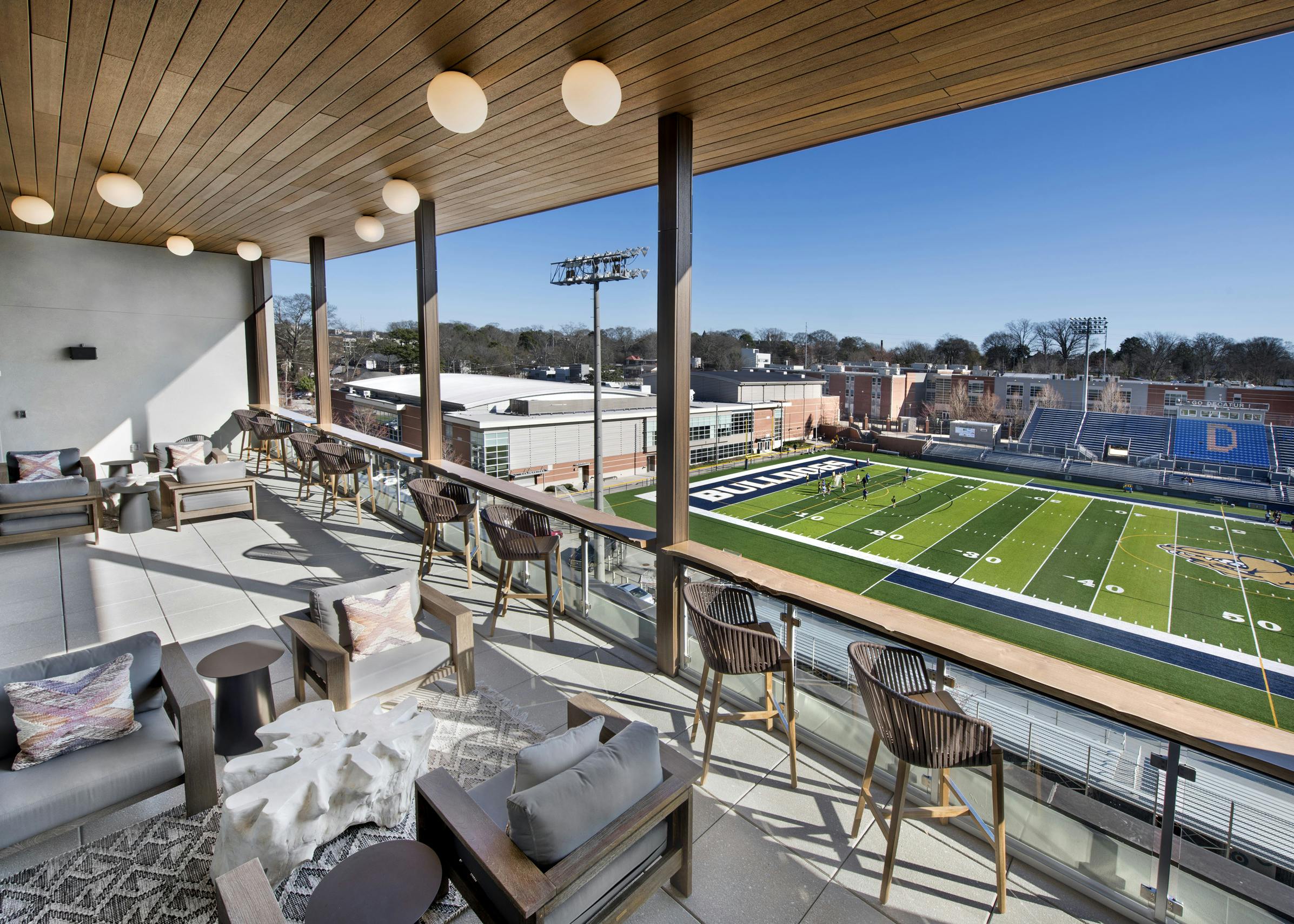 Daytime view of sky lounge deck at AMLI Decatur with multiple seating areas overseeing Decatur Bulldogs football field