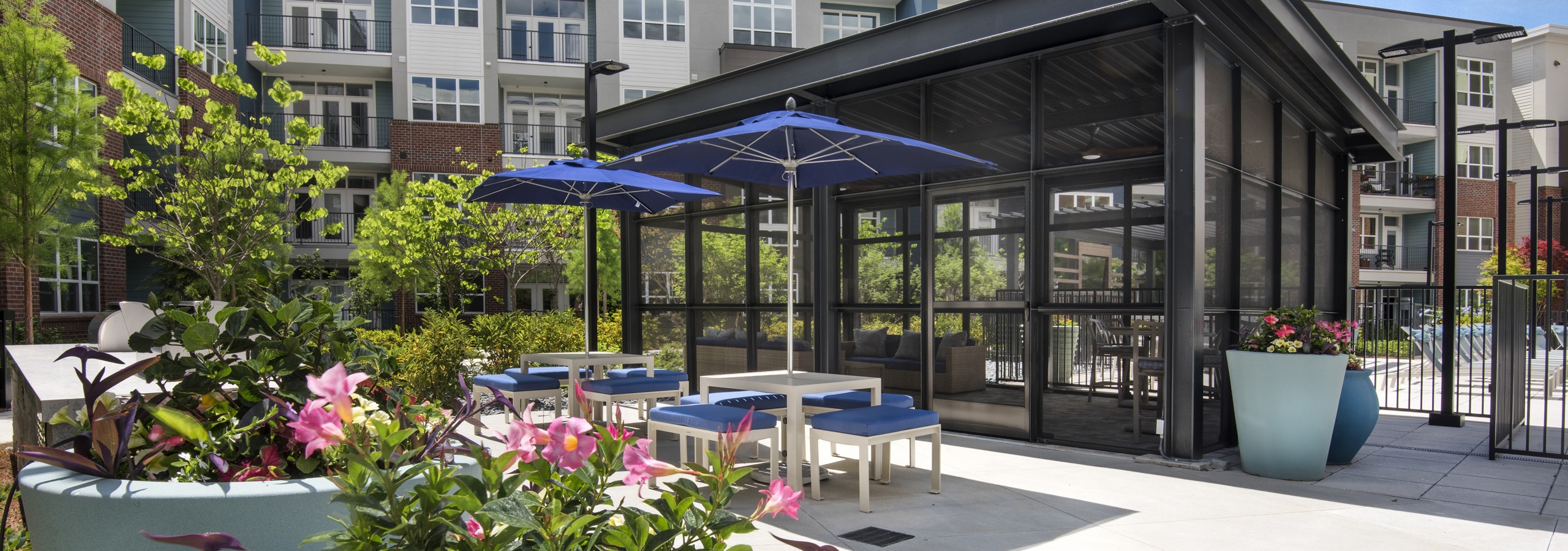 Daytime view of screened pool room at AMLI Decatur apartments  with sofa surrounded with bright pink flowers and tables