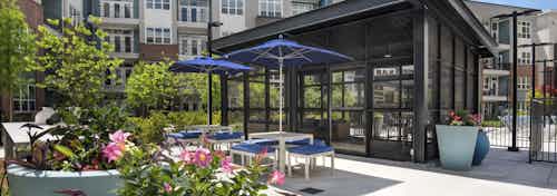 Daytime view of screened pool room at AMLI Decatur apartments with sofa surrounded with bright pink flowers and tables