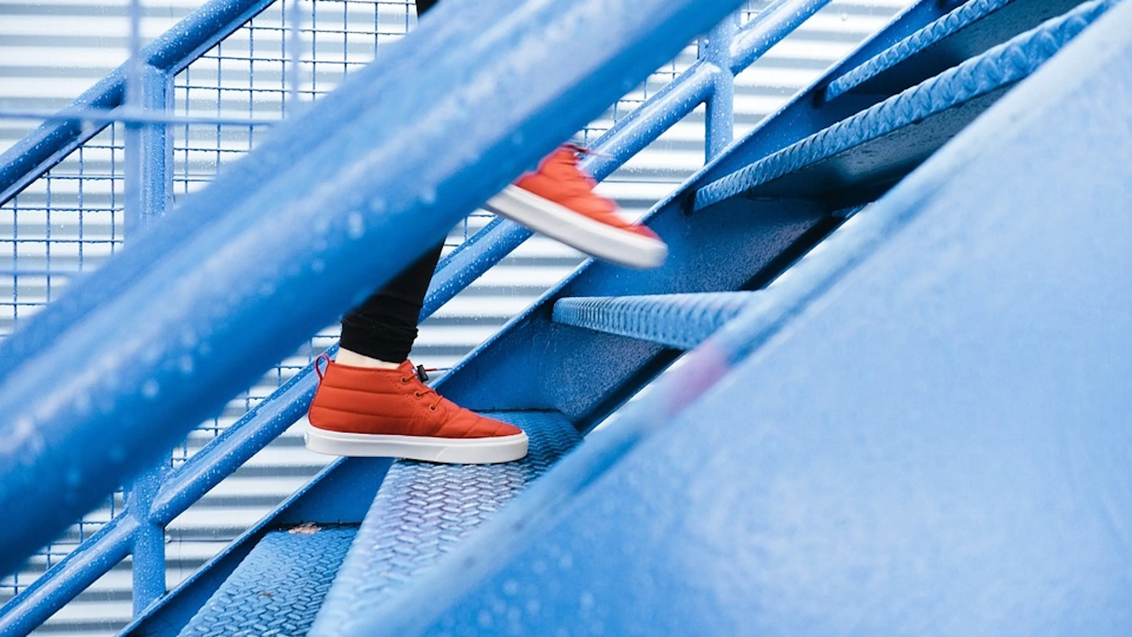 Close up of a pair of bright orange sneakers mid-step going up a blue staircase