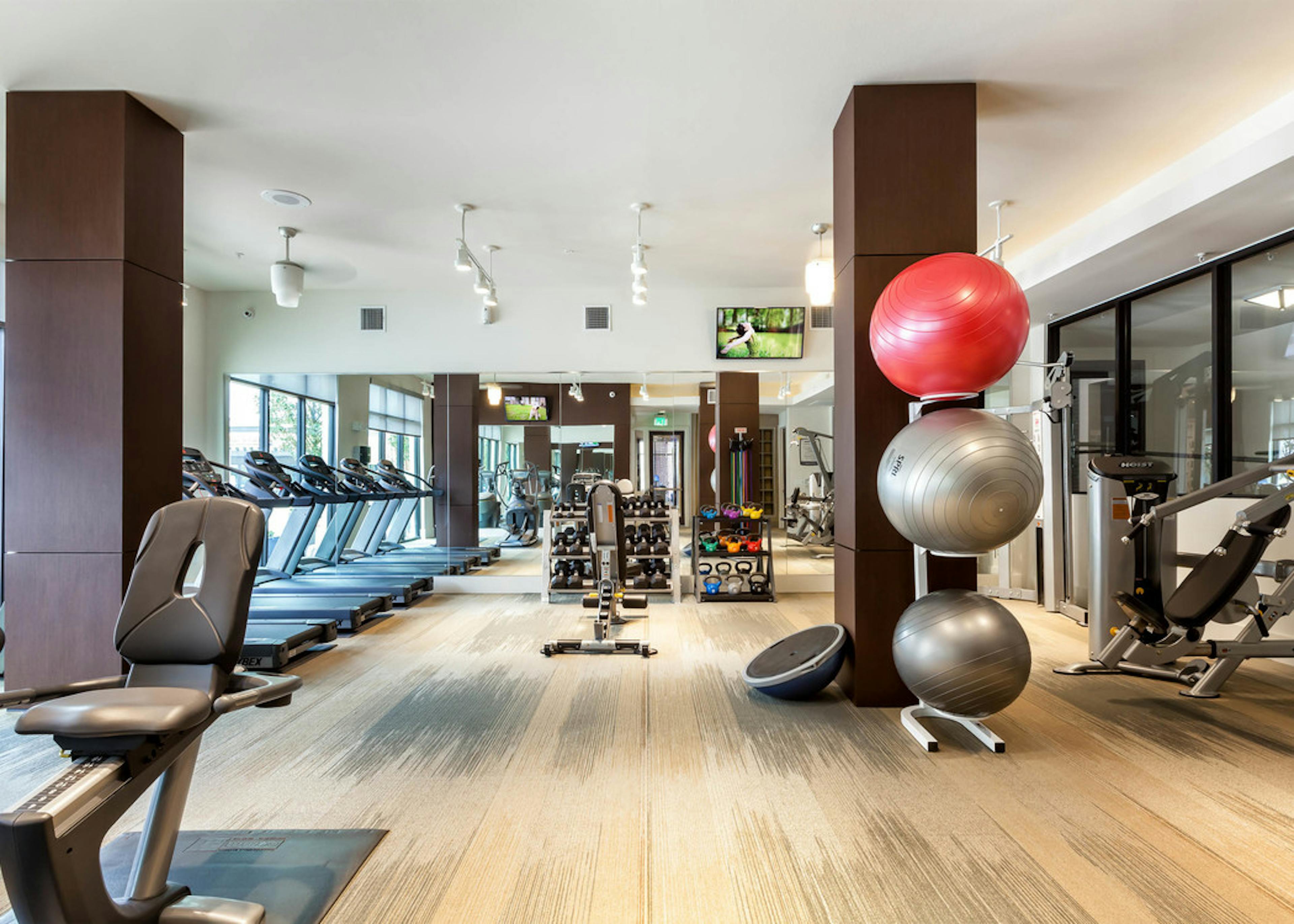 AMLI West Plano fitness center with dark brown pillars and stacked exercise balls with treadmills and dumbbells in background