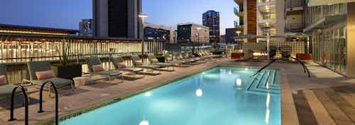 Nighttime view of AMLI Park Broadway swimming pool area with lounge seating overlooking library and Downtown Long Beach